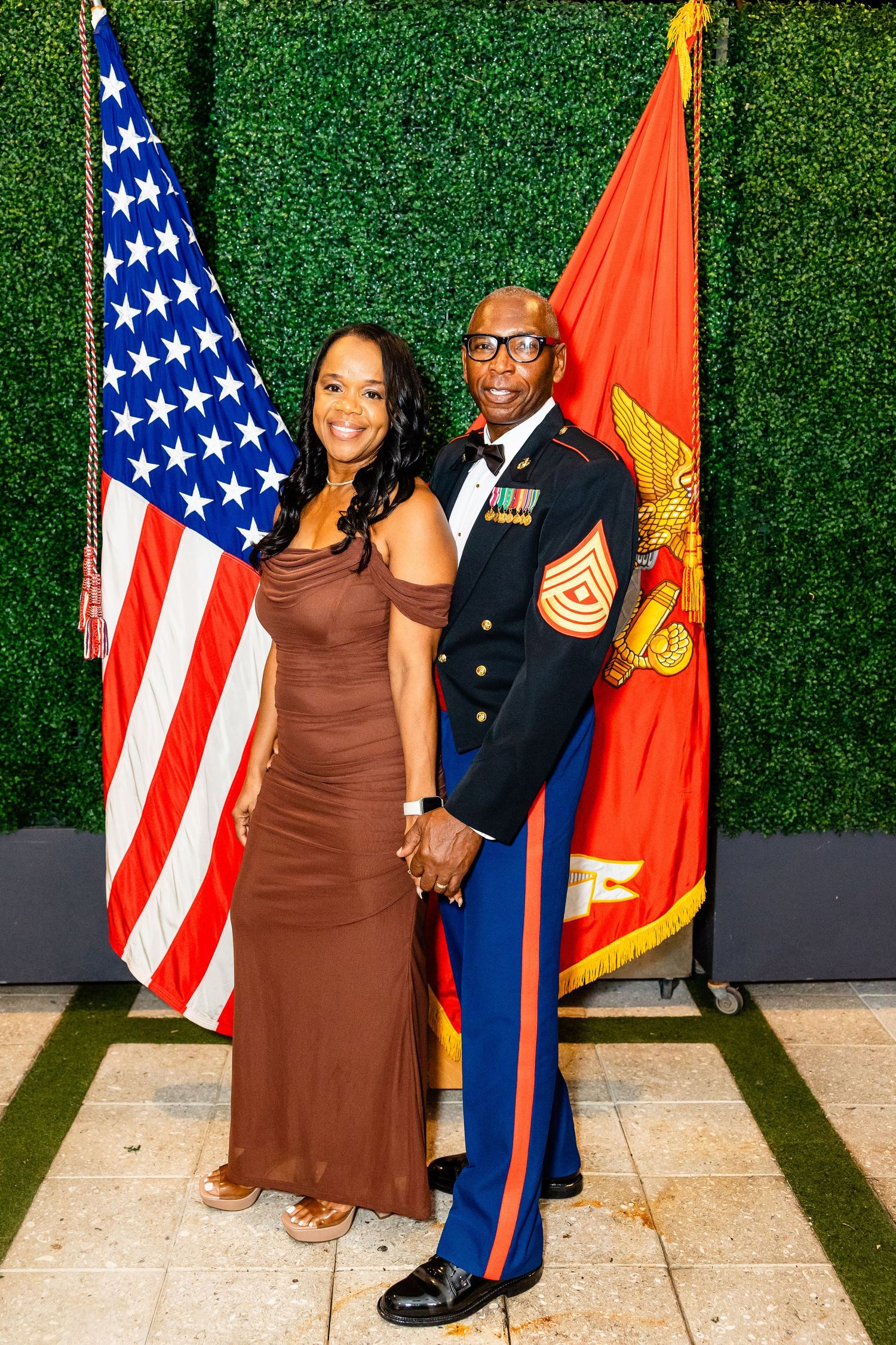 Military personnel and guests pose with flags against a decorative green wall at a formal gathering.