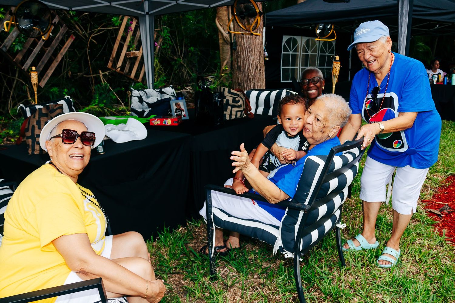 People gathered outdoors for a social gathering with camping chairs and refreshments on a sunny day.