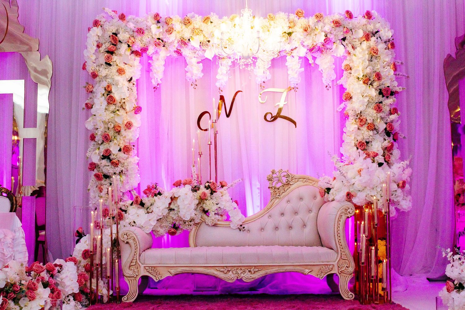Wedding venue with pink uplighting, floral decor and elegant seating arrangement.