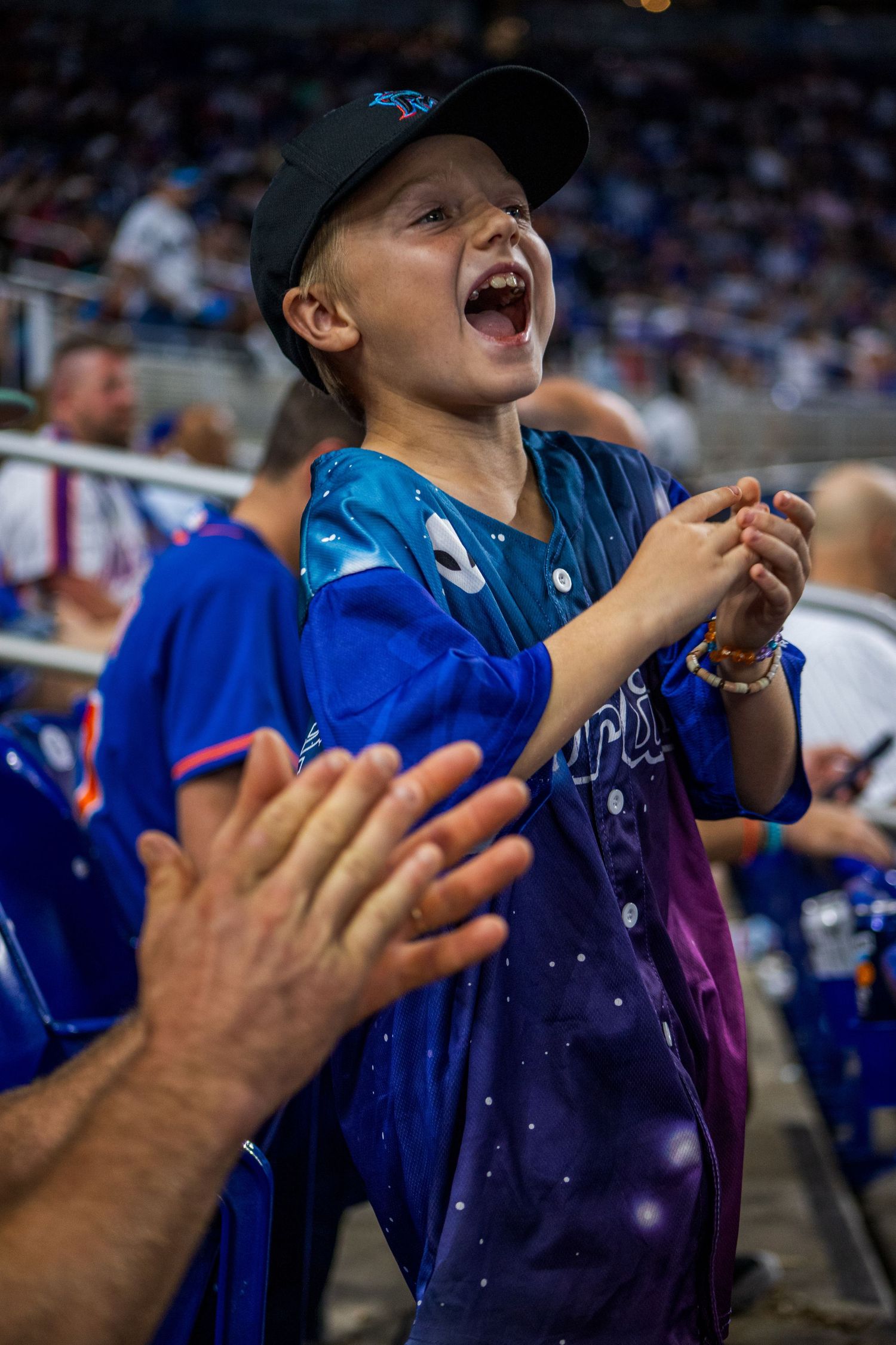 Young baseball fan in a blue jersey reacts with excitement while watching a game at the stadium.