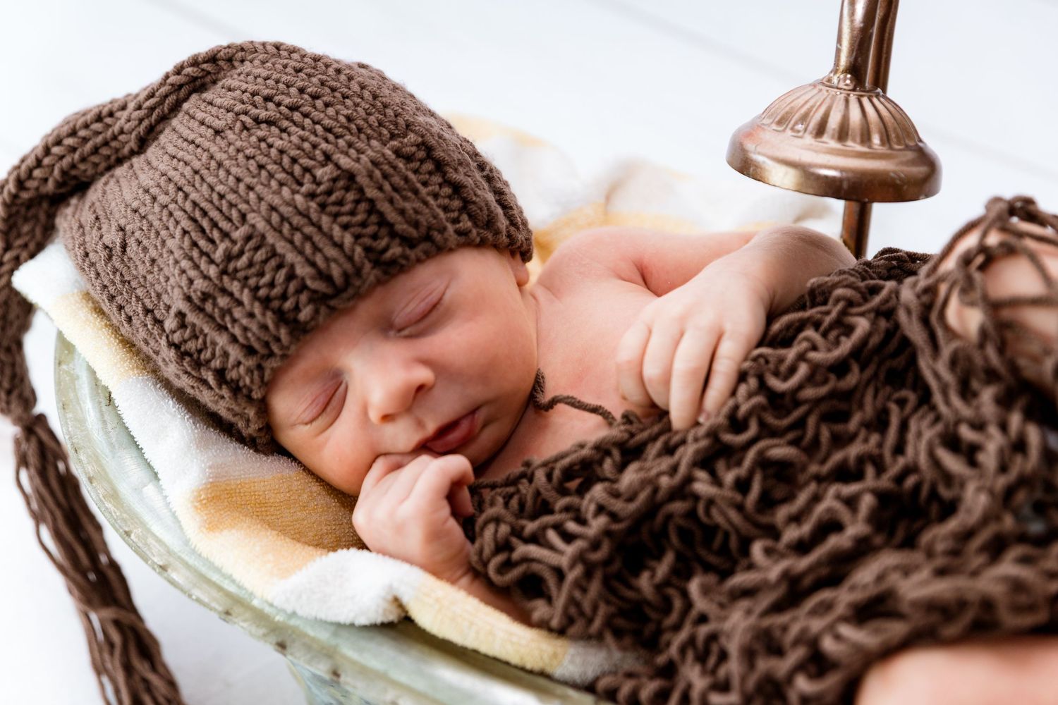 Sleeping newborn swaddled in brown knitted blanket resting in vintage wooden basket.