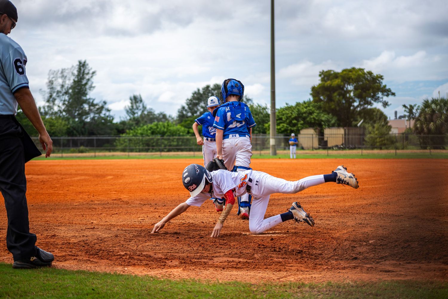 Baseball player makes a dramatic diving catch attempt on a dirt infield during a game.