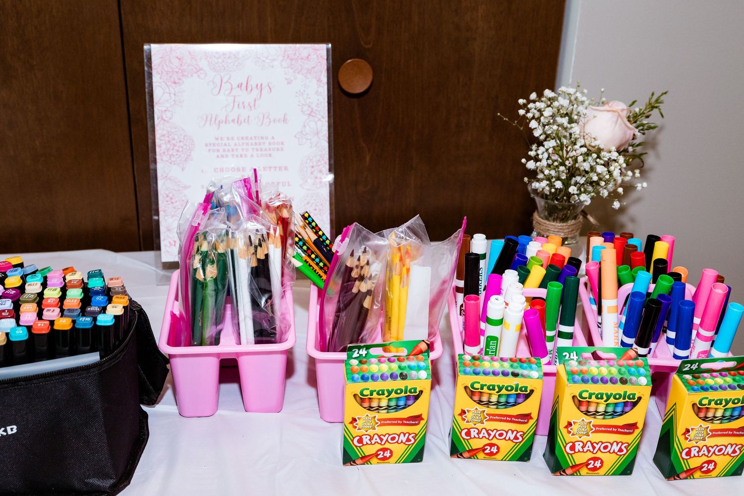 Colorful craft supplies arranged on a table including markers, Crayola crayons, and floral decorations.