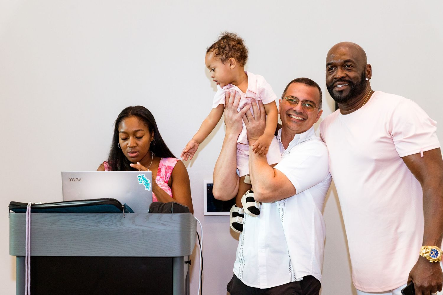 A casual group stands together in a medical office setting with pink accents.