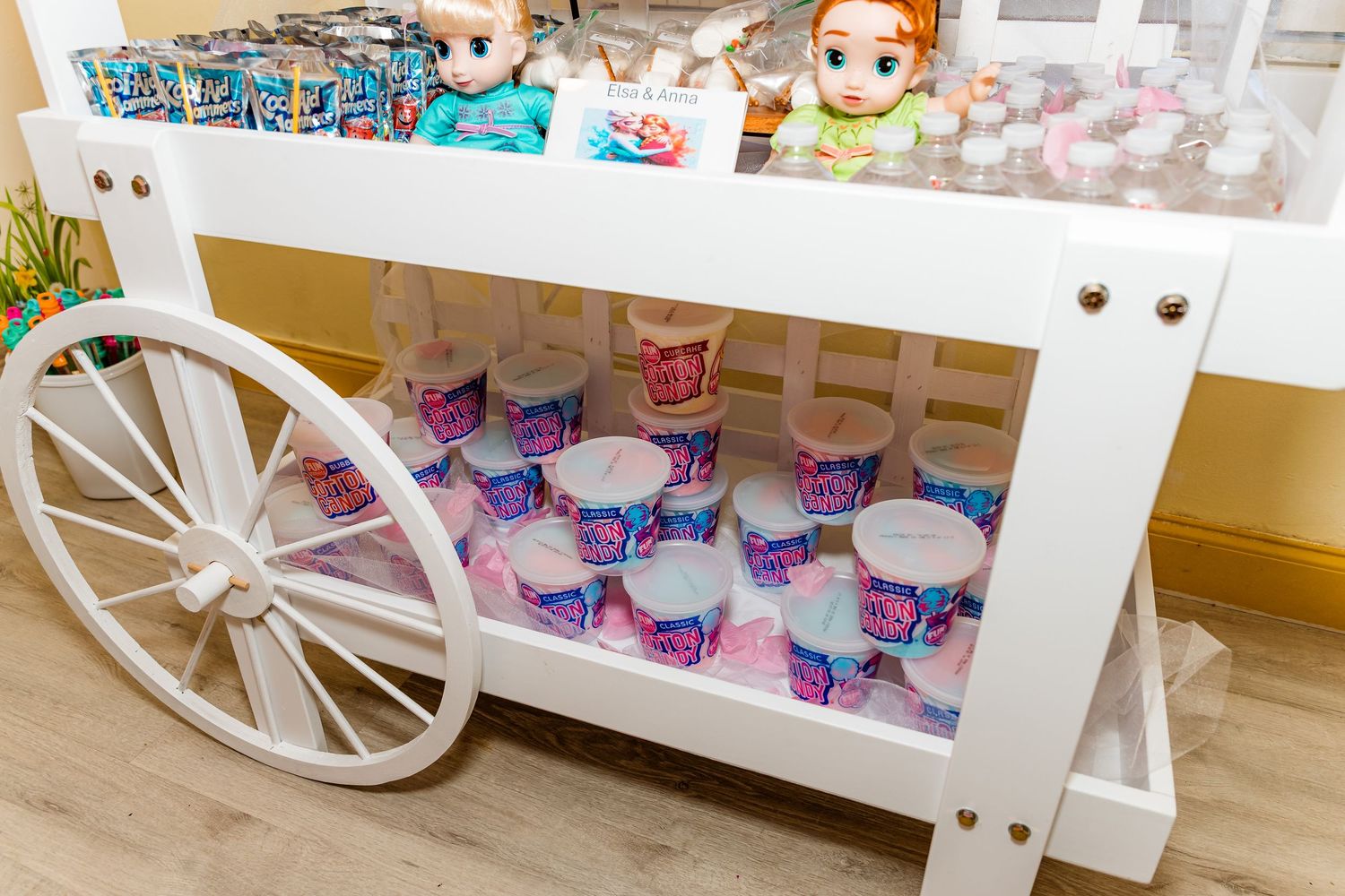 A white decorative cart with wagon wheels displays colorful party favors and treats.