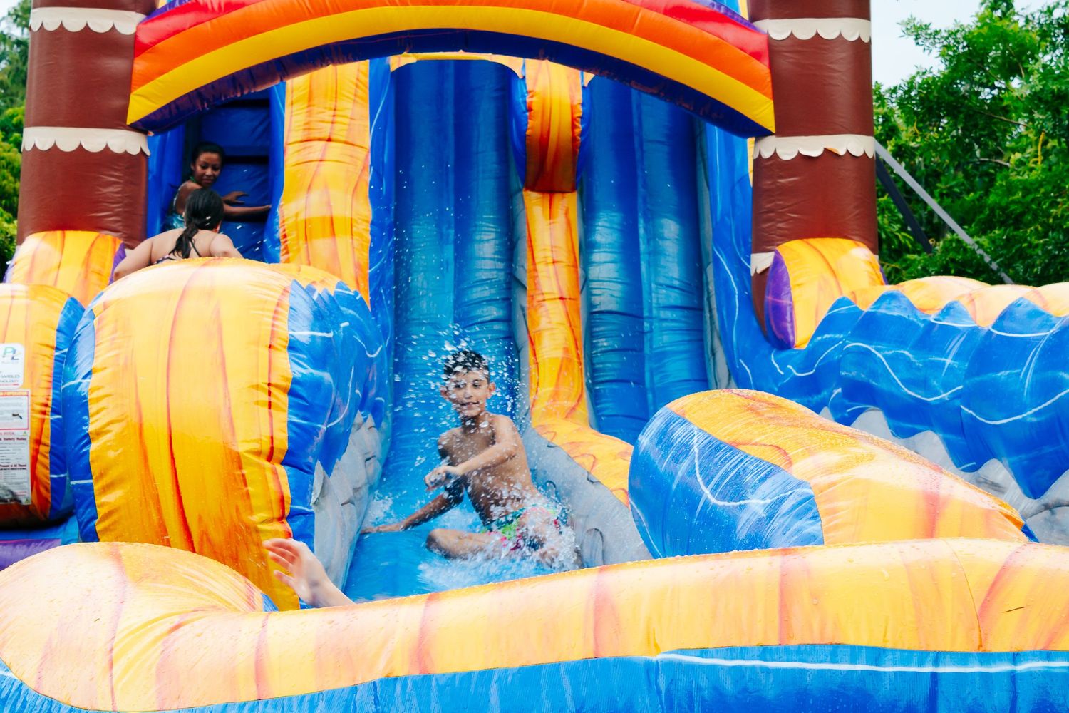 Child sliding down bright inflatable water slide with blue and yellow sections at outdoor party.