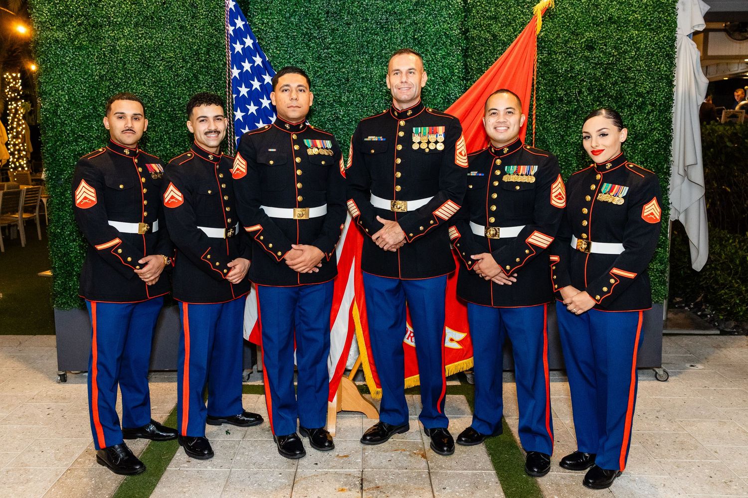 A group in formal Marine Corps dress uniforms pose together at an outdoor event.