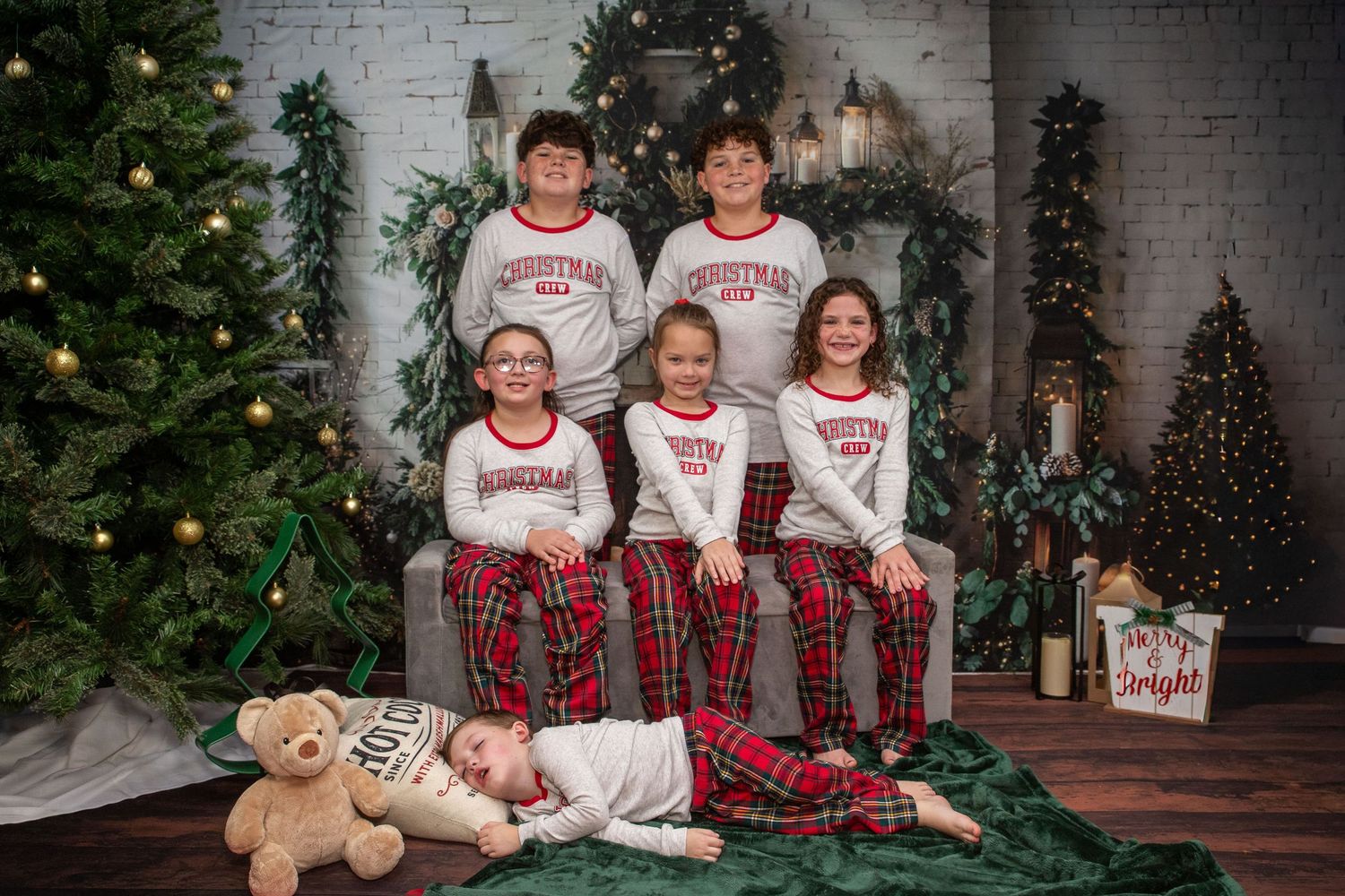 A group wearing matching Christmas pajamas poses by decorated trees and holiday decor in a cozy indoor setting.