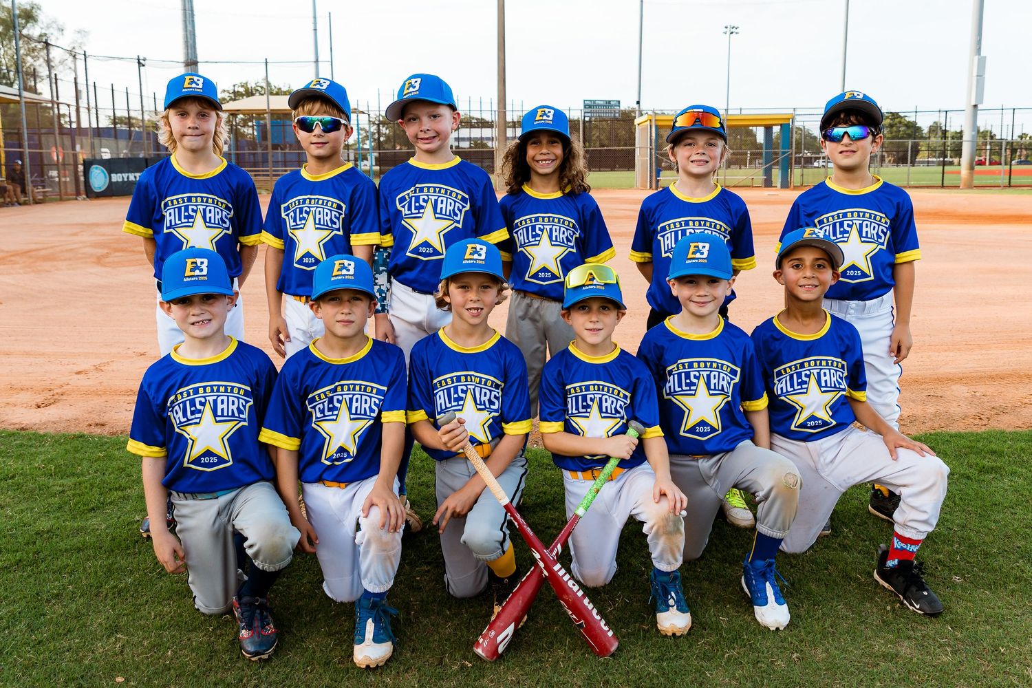Youth baseball team wearing bright blue jerseys poses together on baseball field during team photo day.