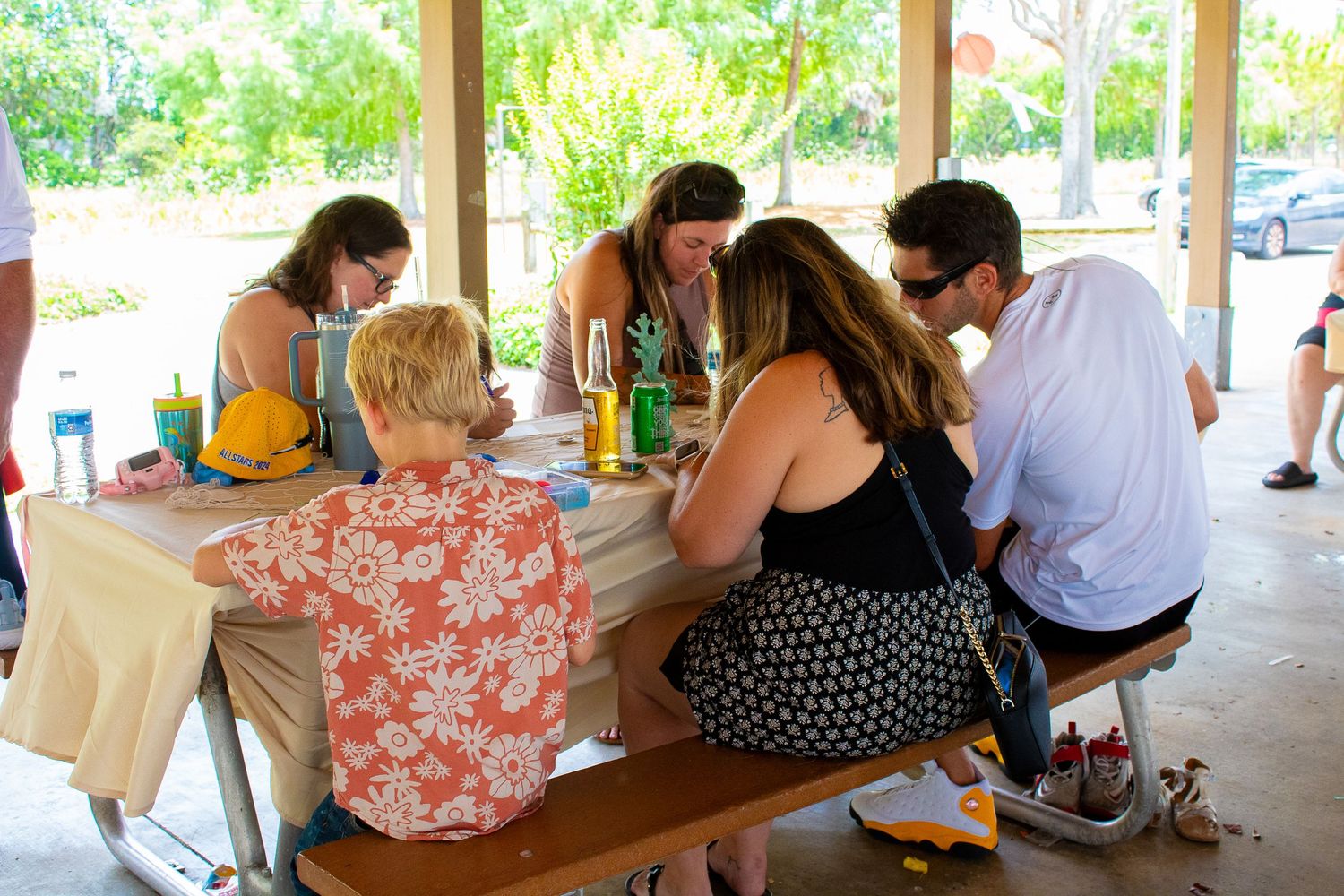 People gathered around picnic table at casual outdoor party under covered shelter.