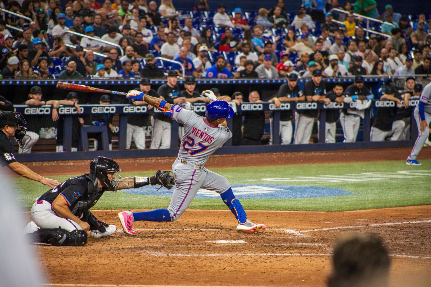 Baseball batter in blue and white uniform swings at pitch while catcher crouches behind home plate.