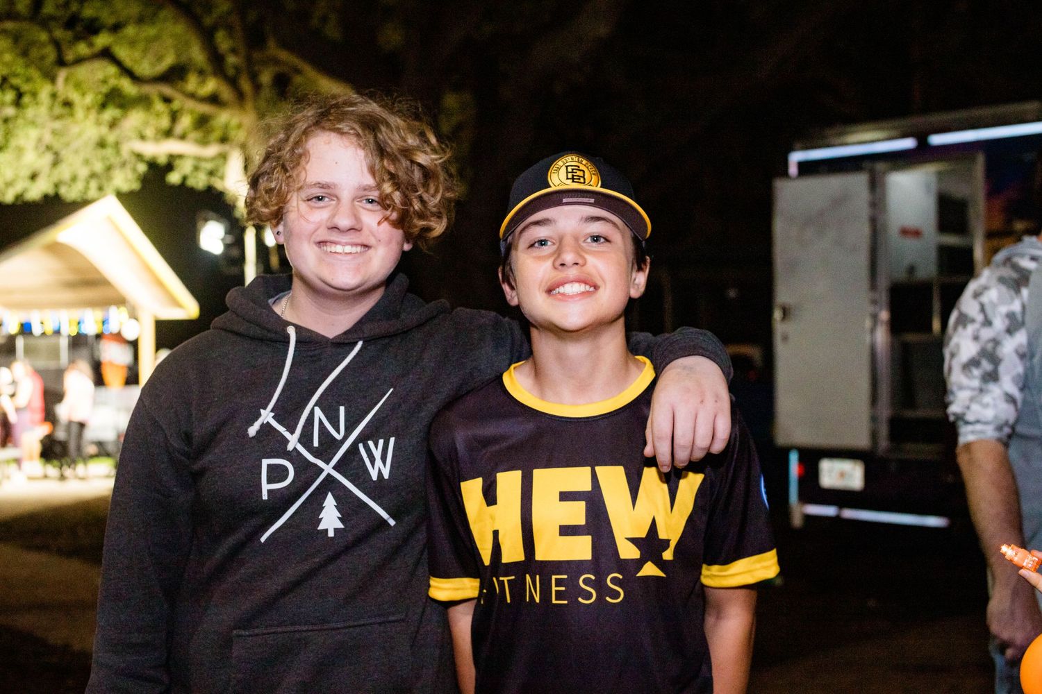 Two young people pose together at a nighttime event, one wearing a baseball cap.
