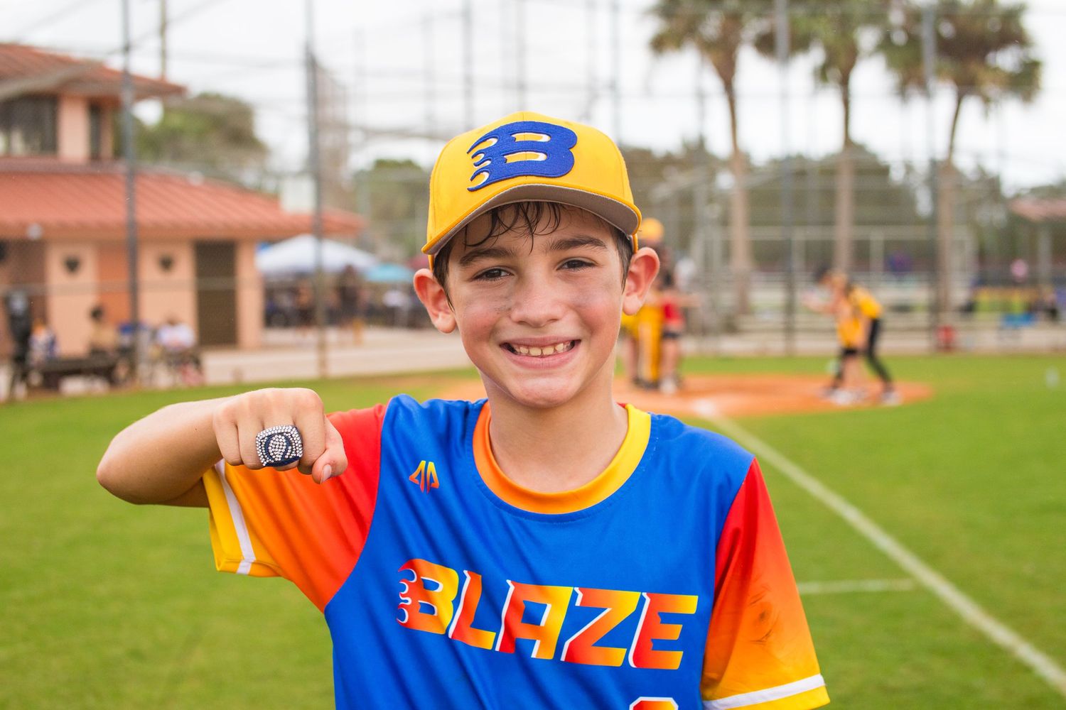 Young baseball player in bright Blaze uniform smiles while displaying team spirit.