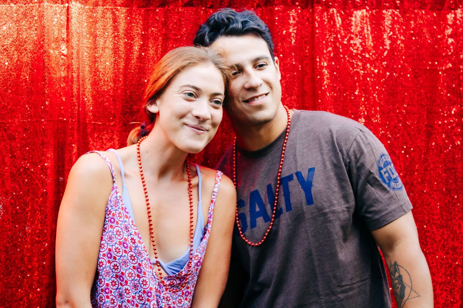 Couple posing in front of a bright red background at an outdoor event.