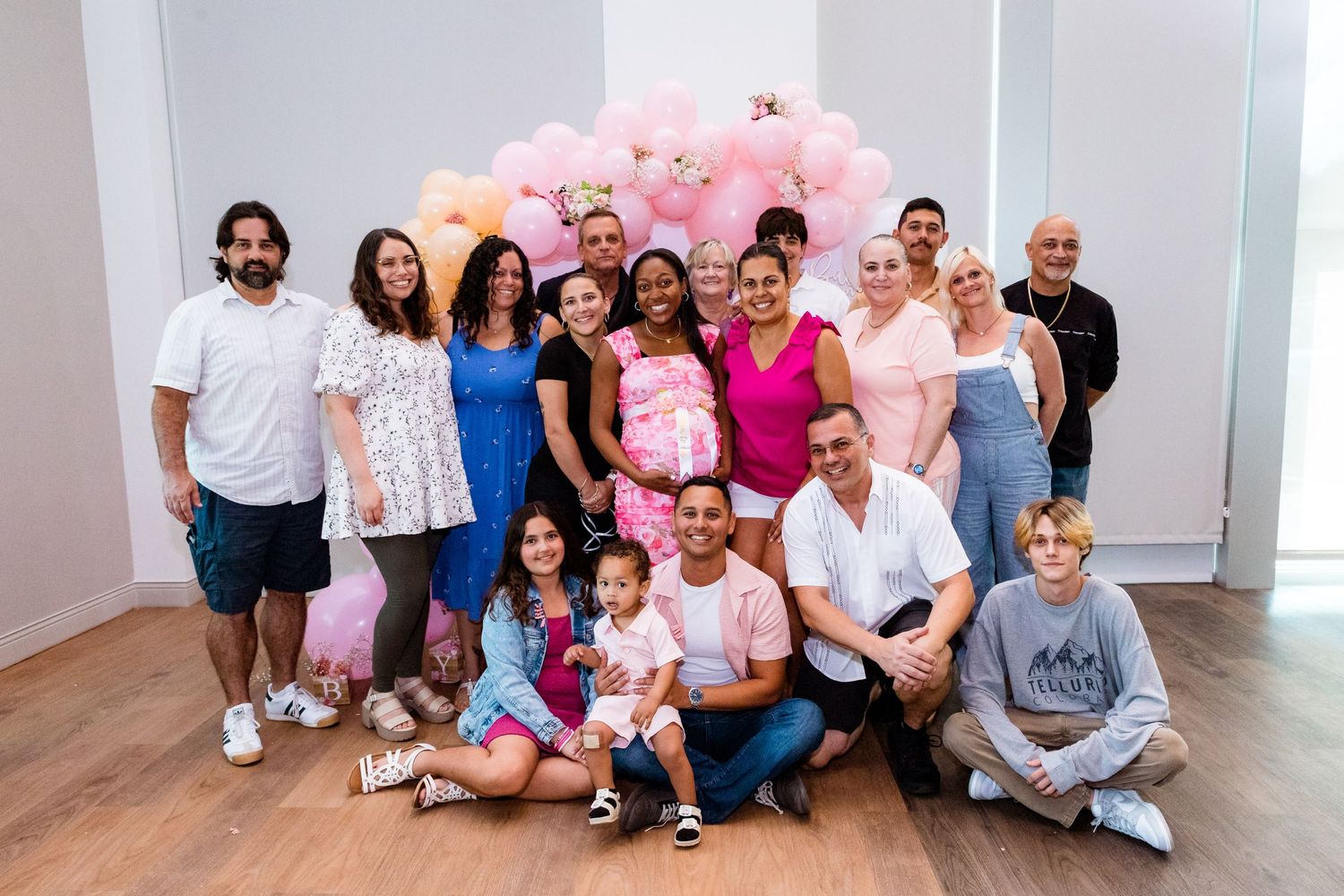 Large group photo of family and friends gathered at a baby shower with balloon decorations.