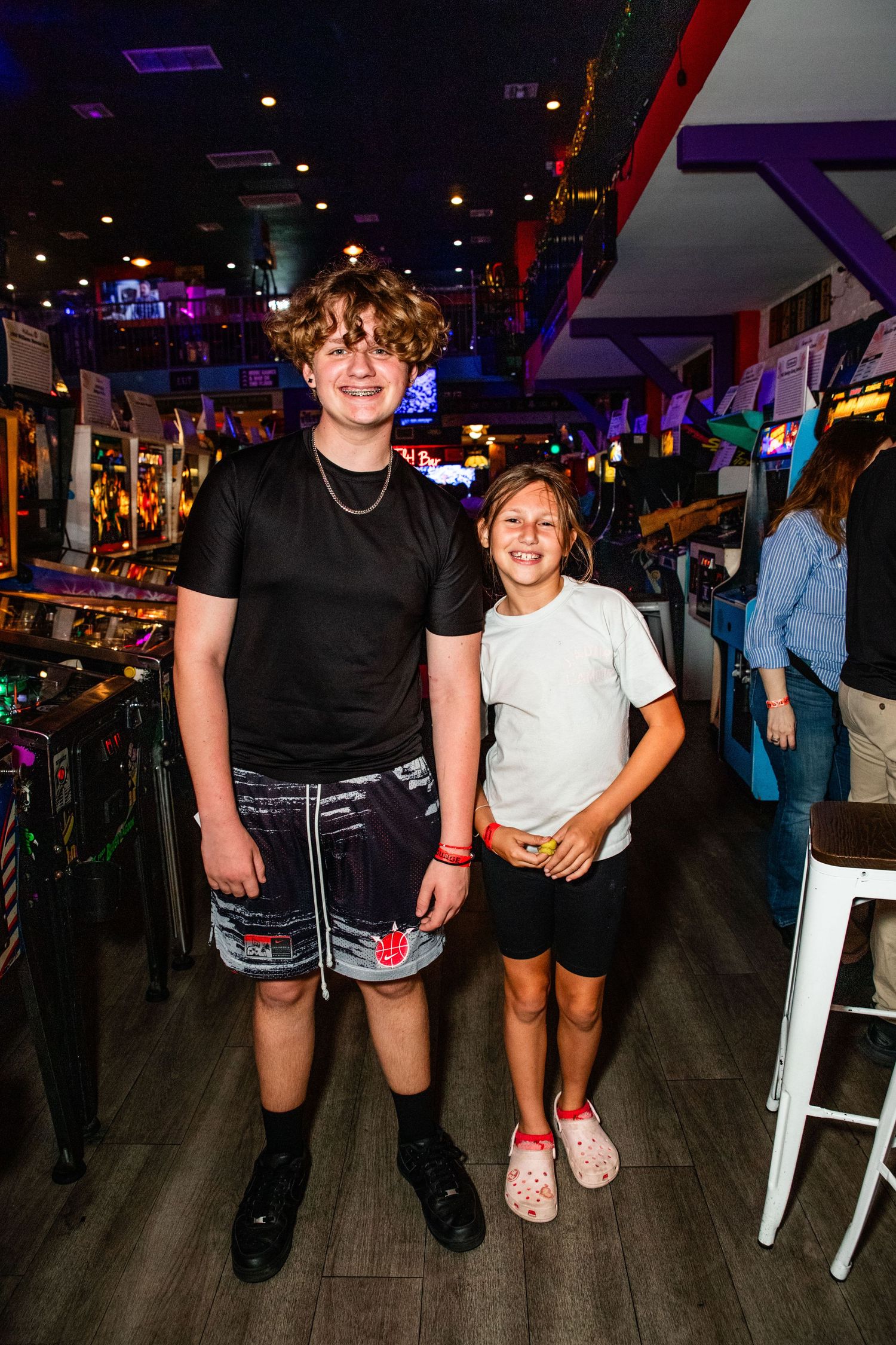 Two young people posing for a photo in an arcade or entertainment center.