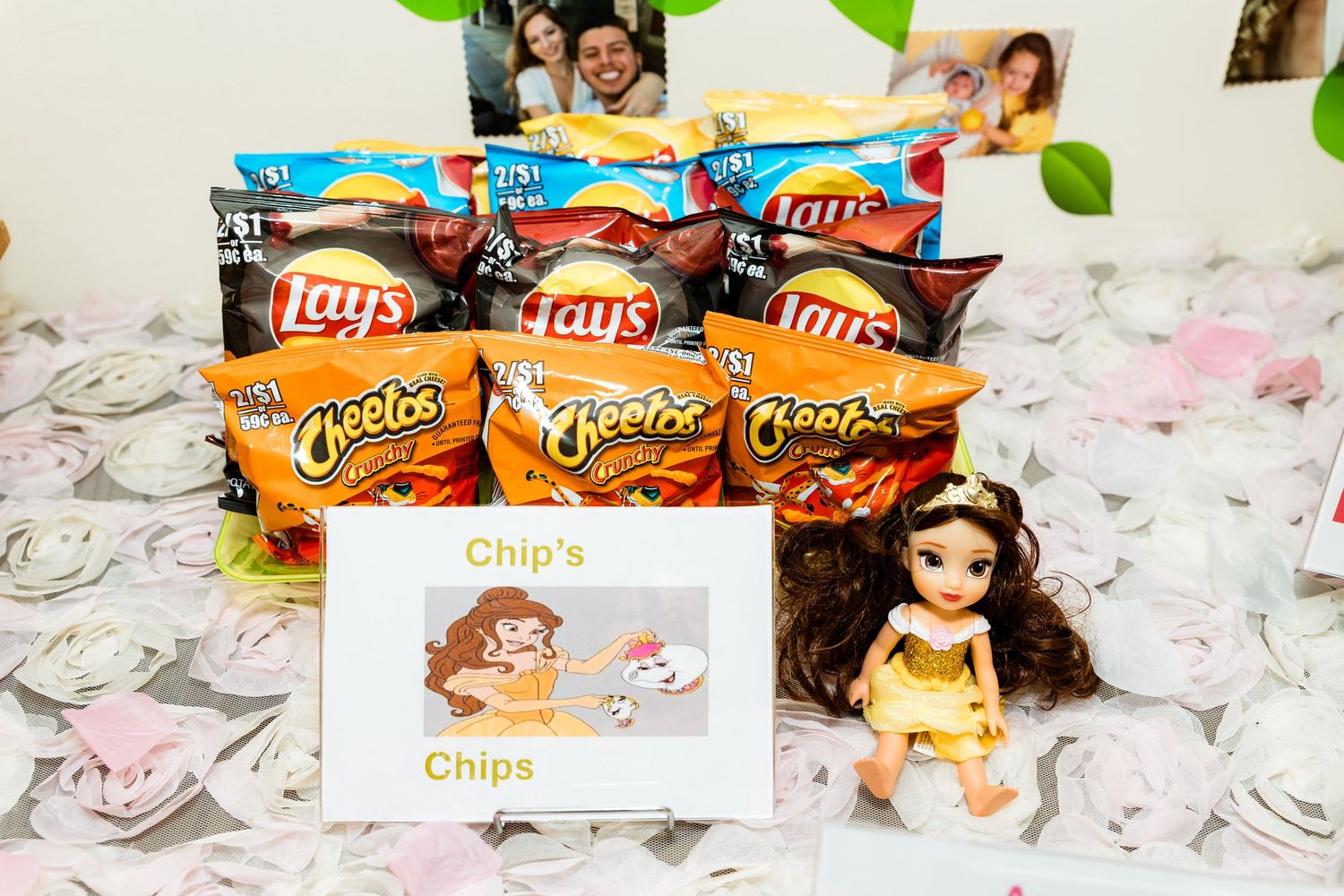 Snack table setup with chips and other party foods arranged with decorative pink and white elements.