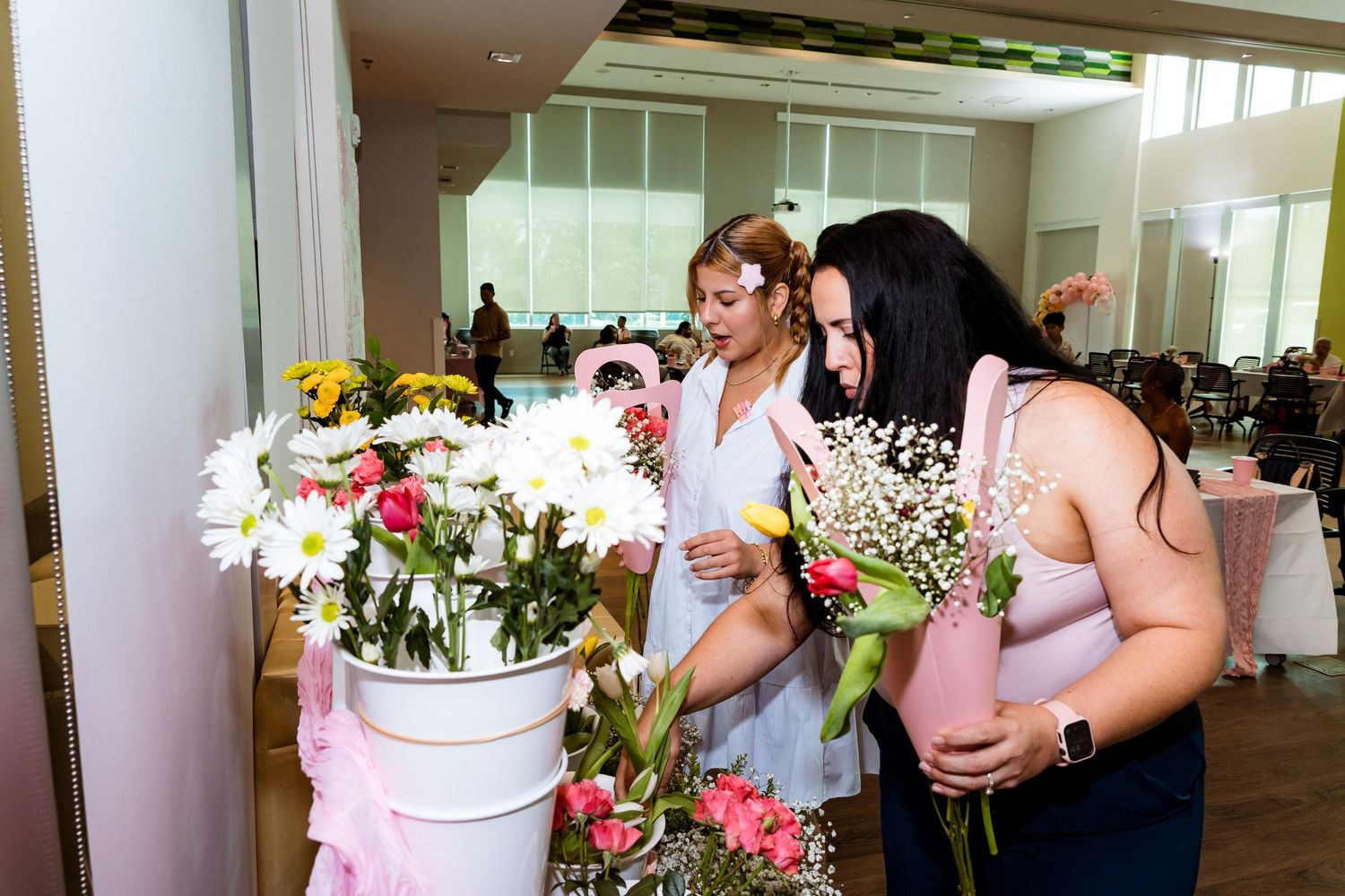 Indoor gathering with people handling floral arrangements and white buckets.