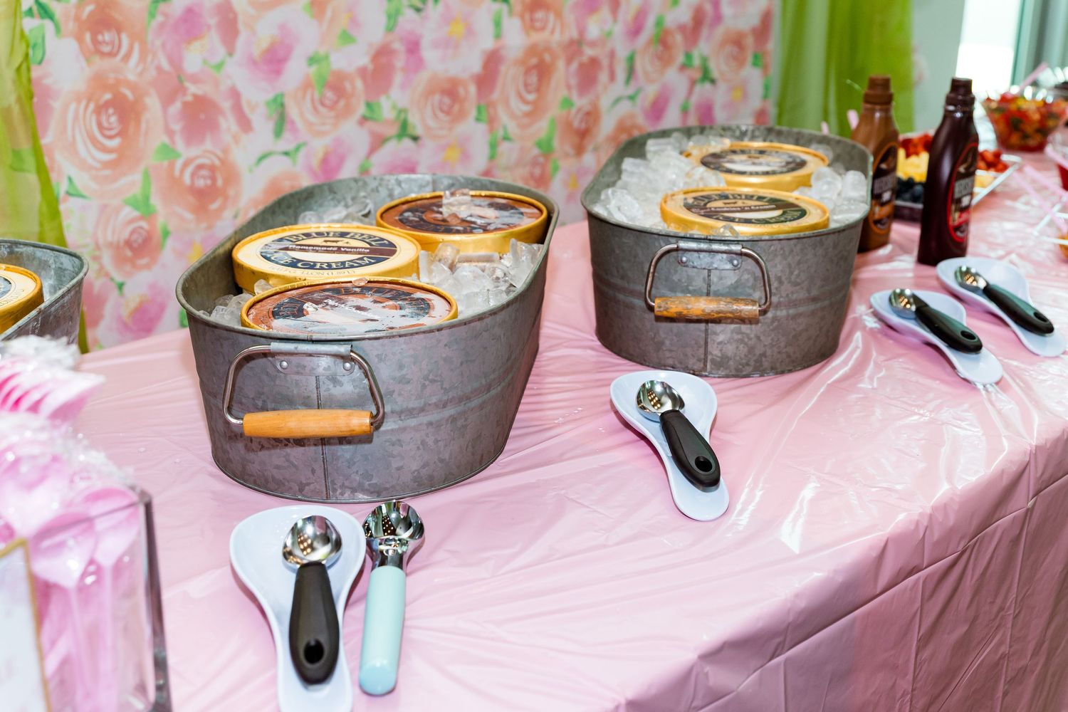 Chafing dishes with food warmers arranged on a pink tablecloth with floral wallpaper background.