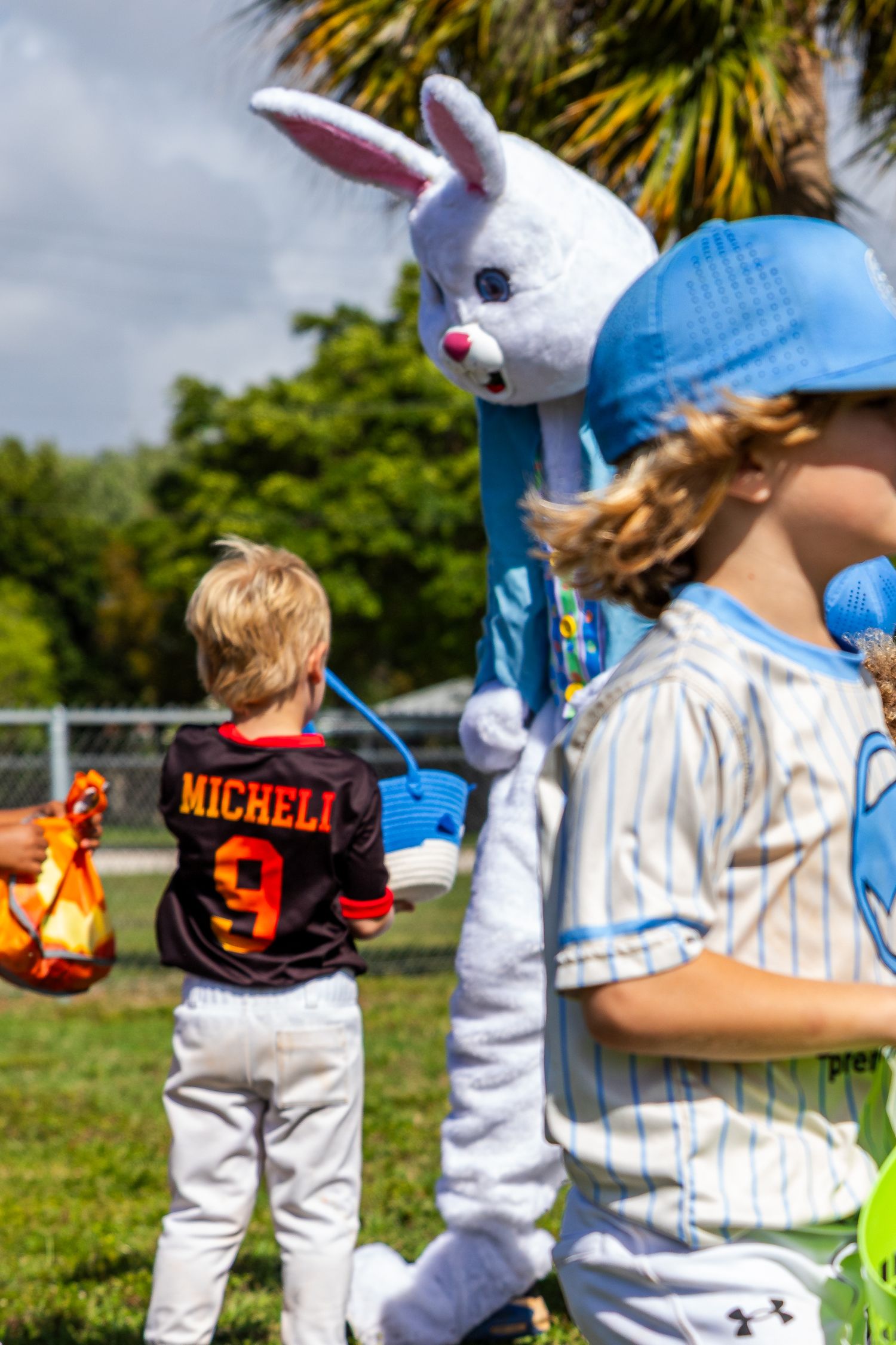 Children in baseball jerseys meet the Easter Bunny mascot outdoors at a sunny spring baseball event in Florida.