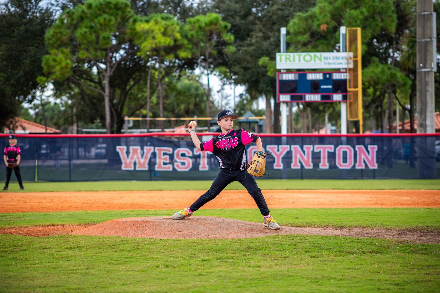 Baseball game in progress on well-maintained field with dugout and fence visible.