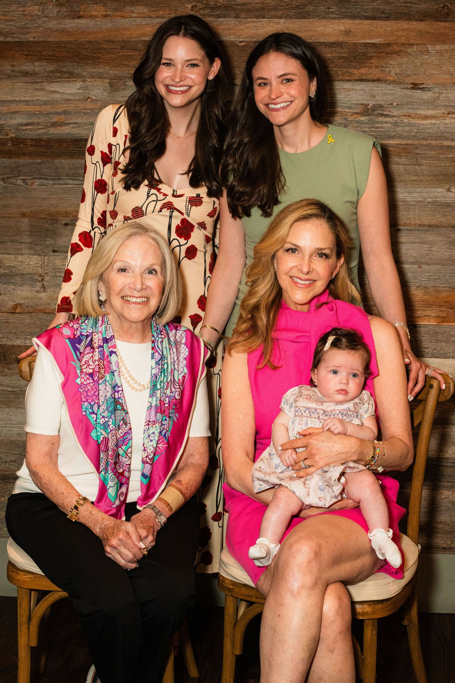Multi-generational family portrait with baby against rustic wood background wearing colorful outfits.