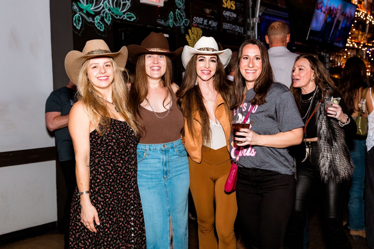 Five friends in western-themed outfits smiling together at party venue.