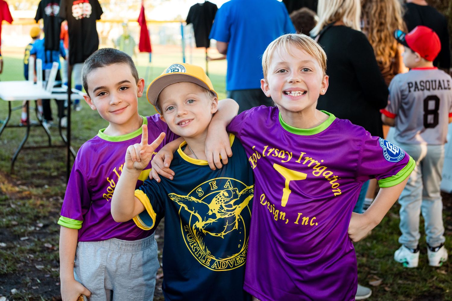 Three young fans in sports jerseys pose together at outdoor event.