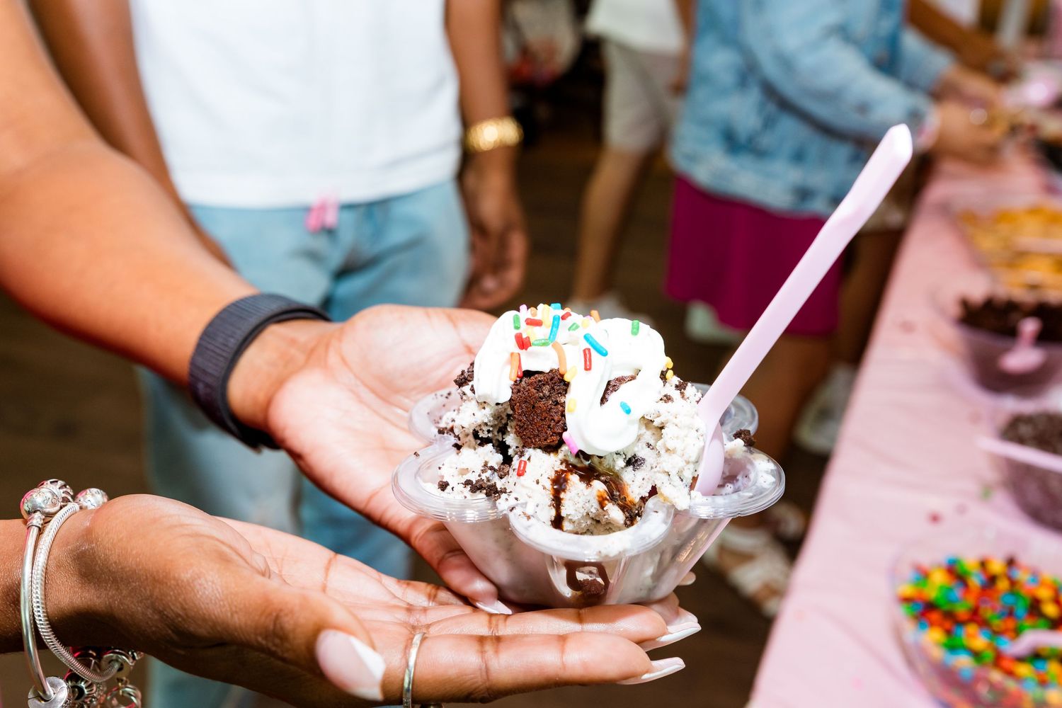 A decorated ice cream sundae with toppings and whipped cream held in someone's hand.
