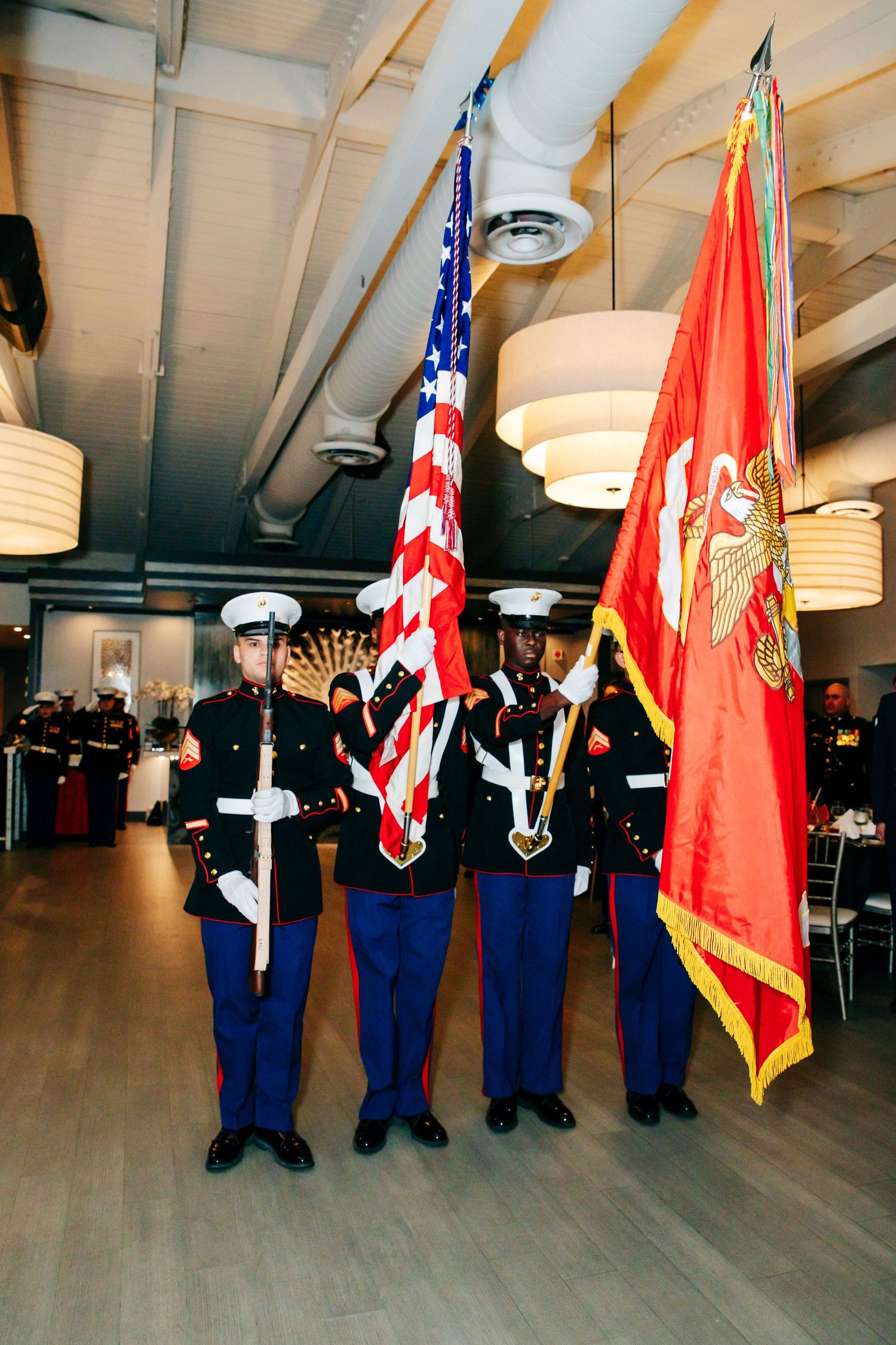 Color guard members in Marine dress uniforms stand at attention holding American and Marine Corps flags.