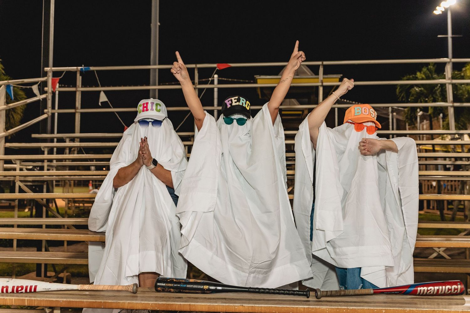 People in ghost costumes create a wave effect across stadium seating at night.