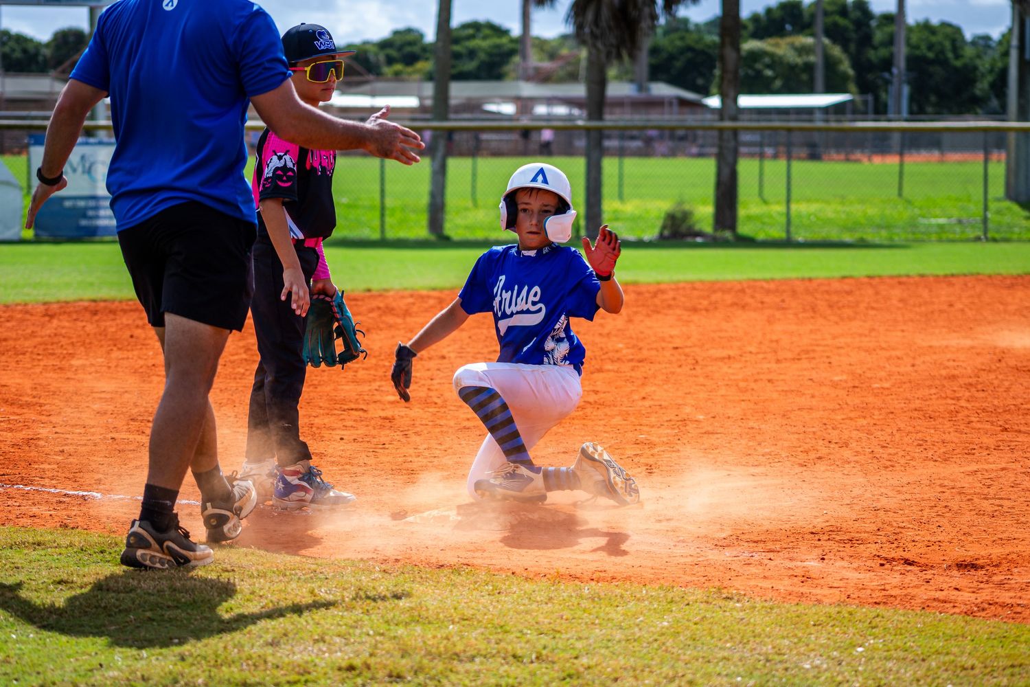 Baseball player slides into base creating a cloud of orange dirt on the infield during an intense game.