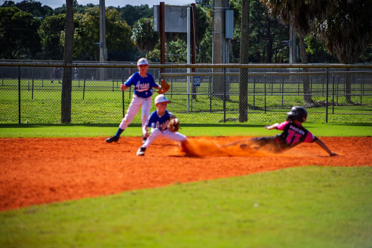 Baseball player sliding into base on orange dirt infield during game at outdoor sports field.