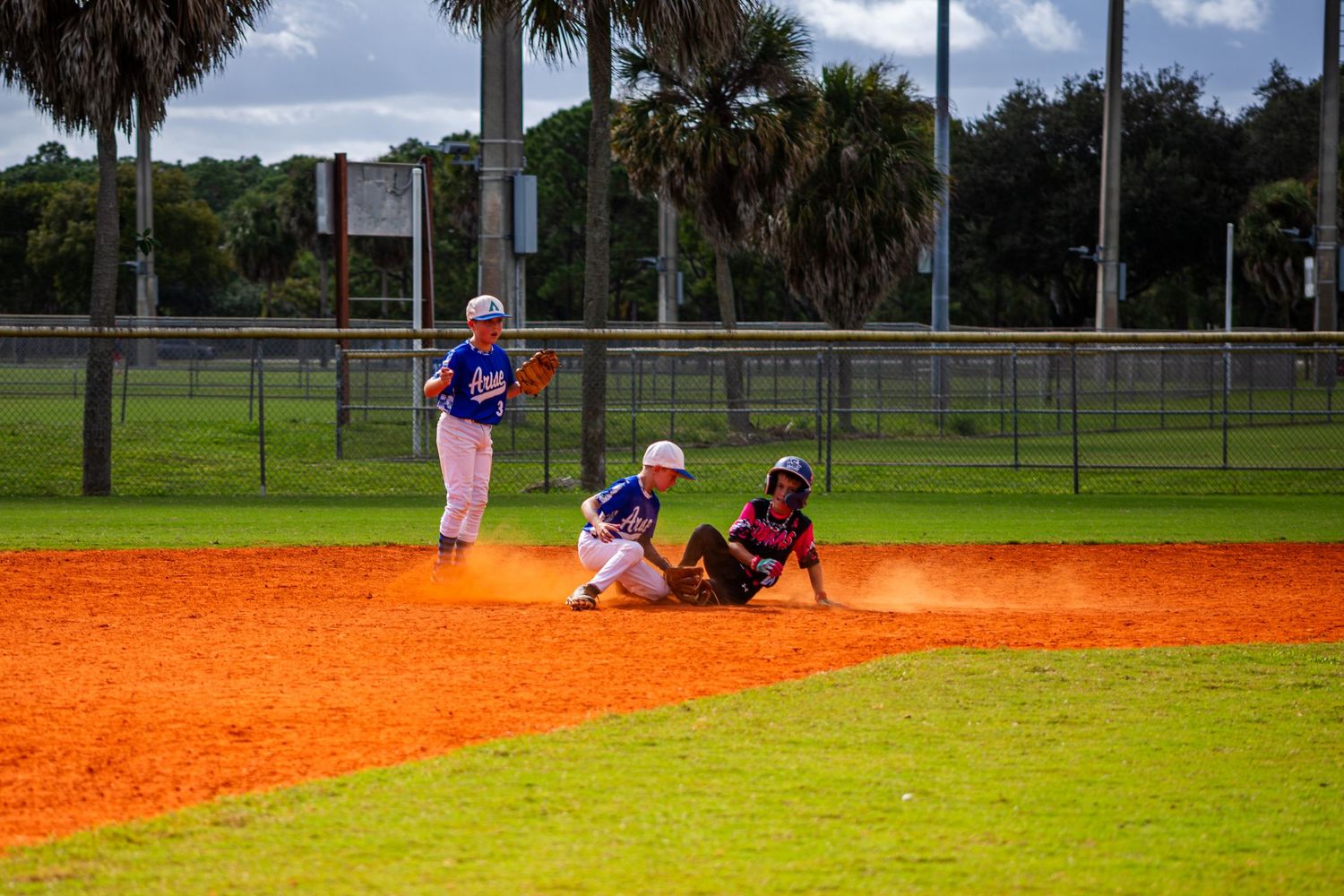 Youth baseball players in action on a bright orange clay baseball field during a sunny day.