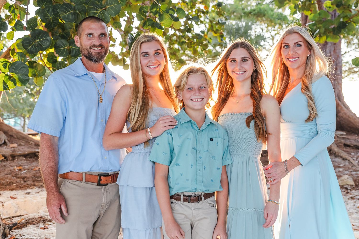 Family group wearing coordinated light blue and mint colored outfits posing together outdoors.