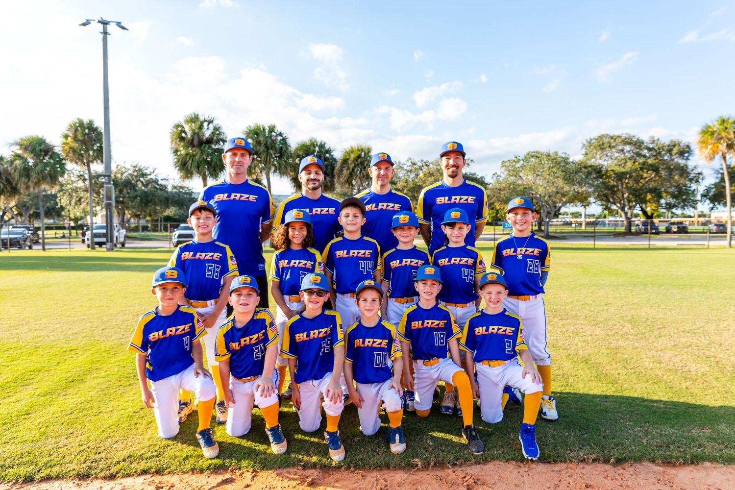 Baseball team in blue uniforms poses together on sunny field for team photo.