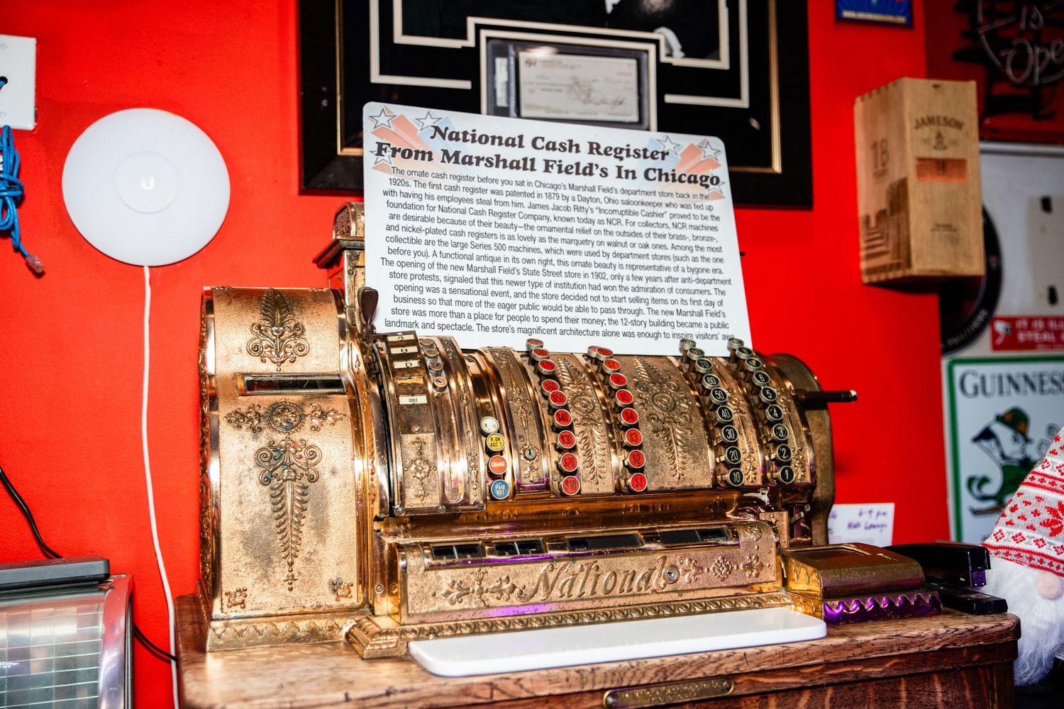 A vintage cash register with ornate designs and buttons sits on a counter against a red background.