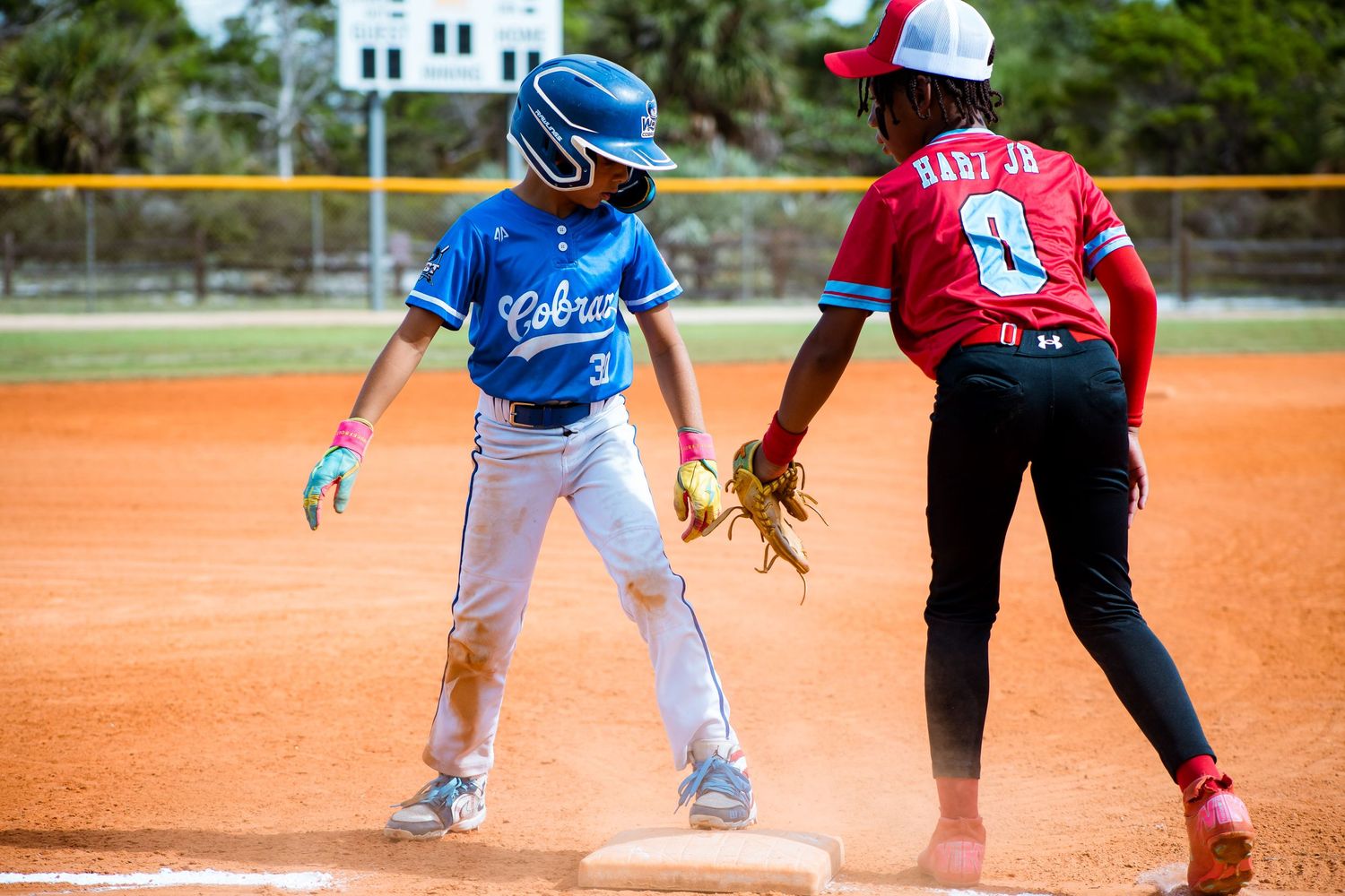 Youth baseball players in red and blue uniforms positioned around the infield during a game.