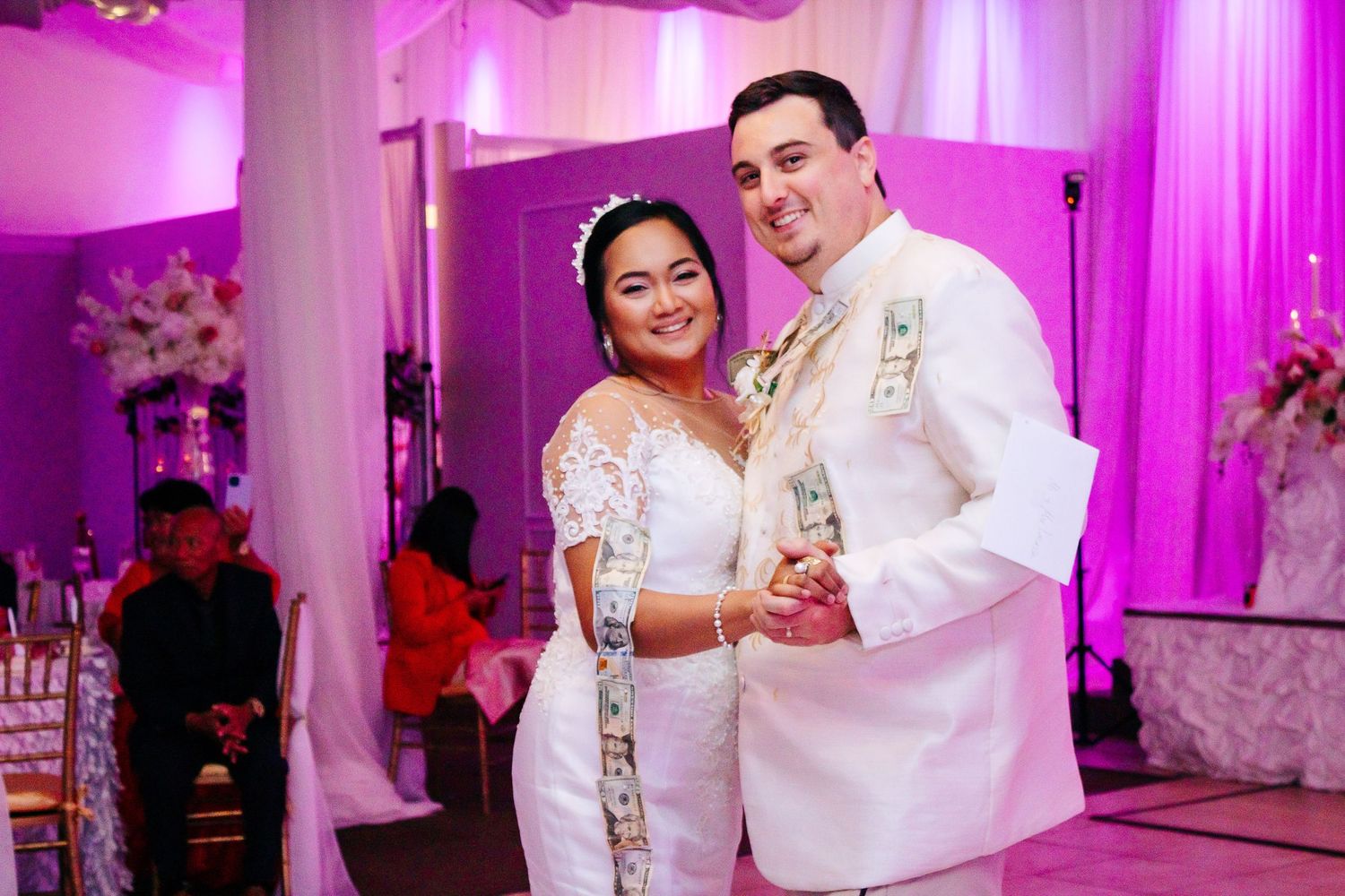 Wedding celebration in a ballroom with pink and purple mood lighting and white drapery.