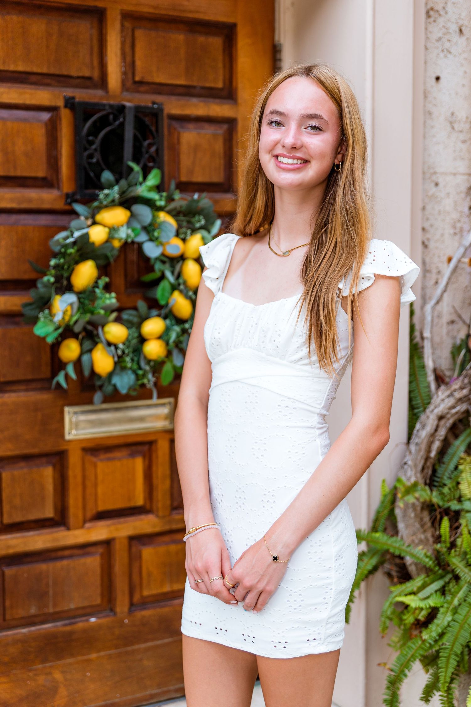 White eyelet dress shown against wooden door with decorative lemon wreath.