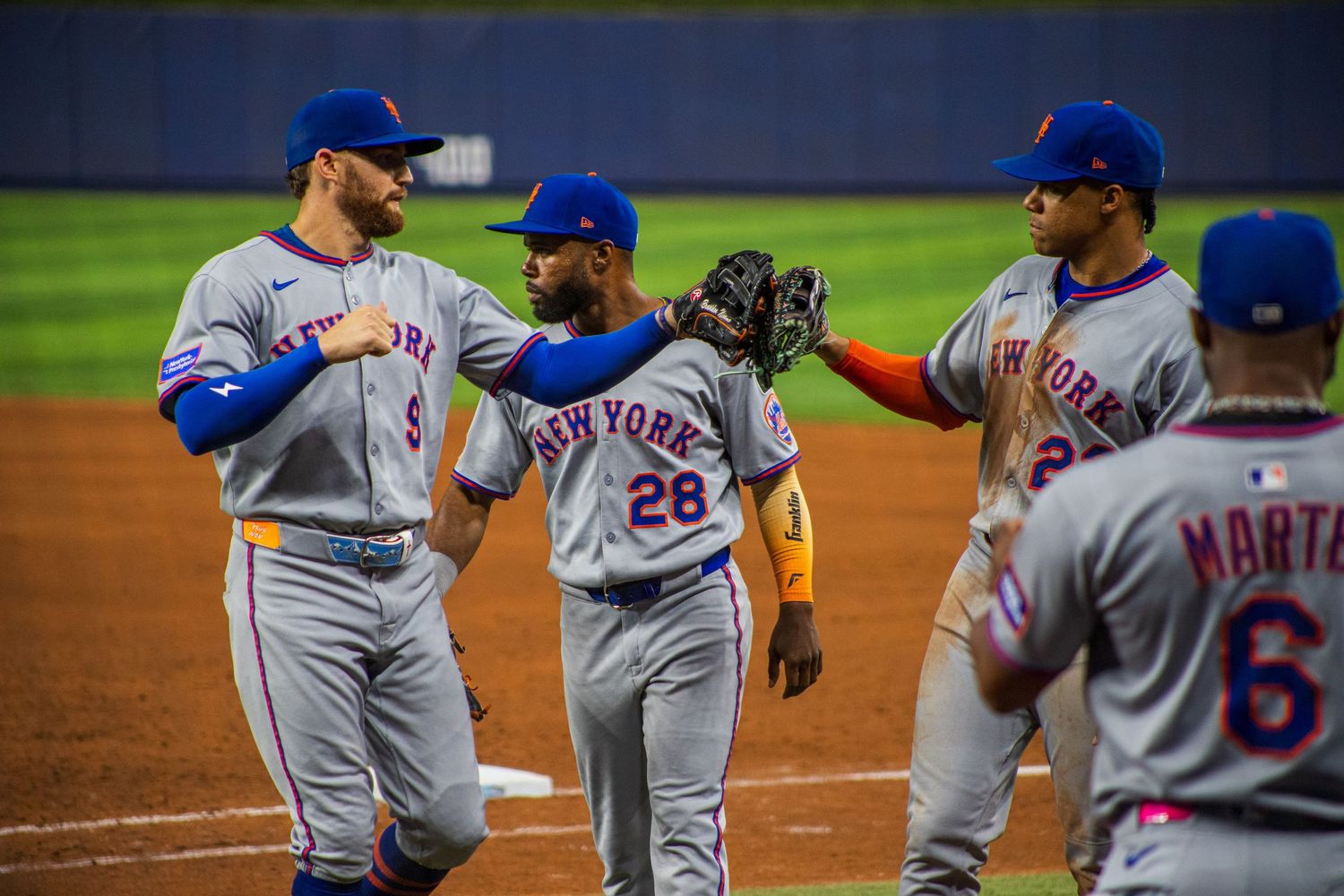 Baseball players in white uniforms gather on field during game for team discussion.
