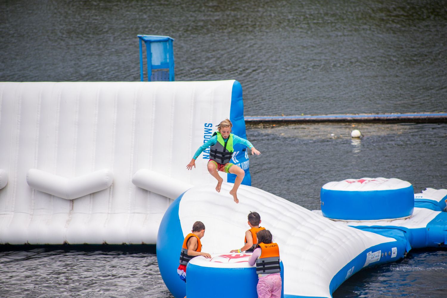 People enjoying a floating water park with inflatable obstacle courses and slides on a lake.