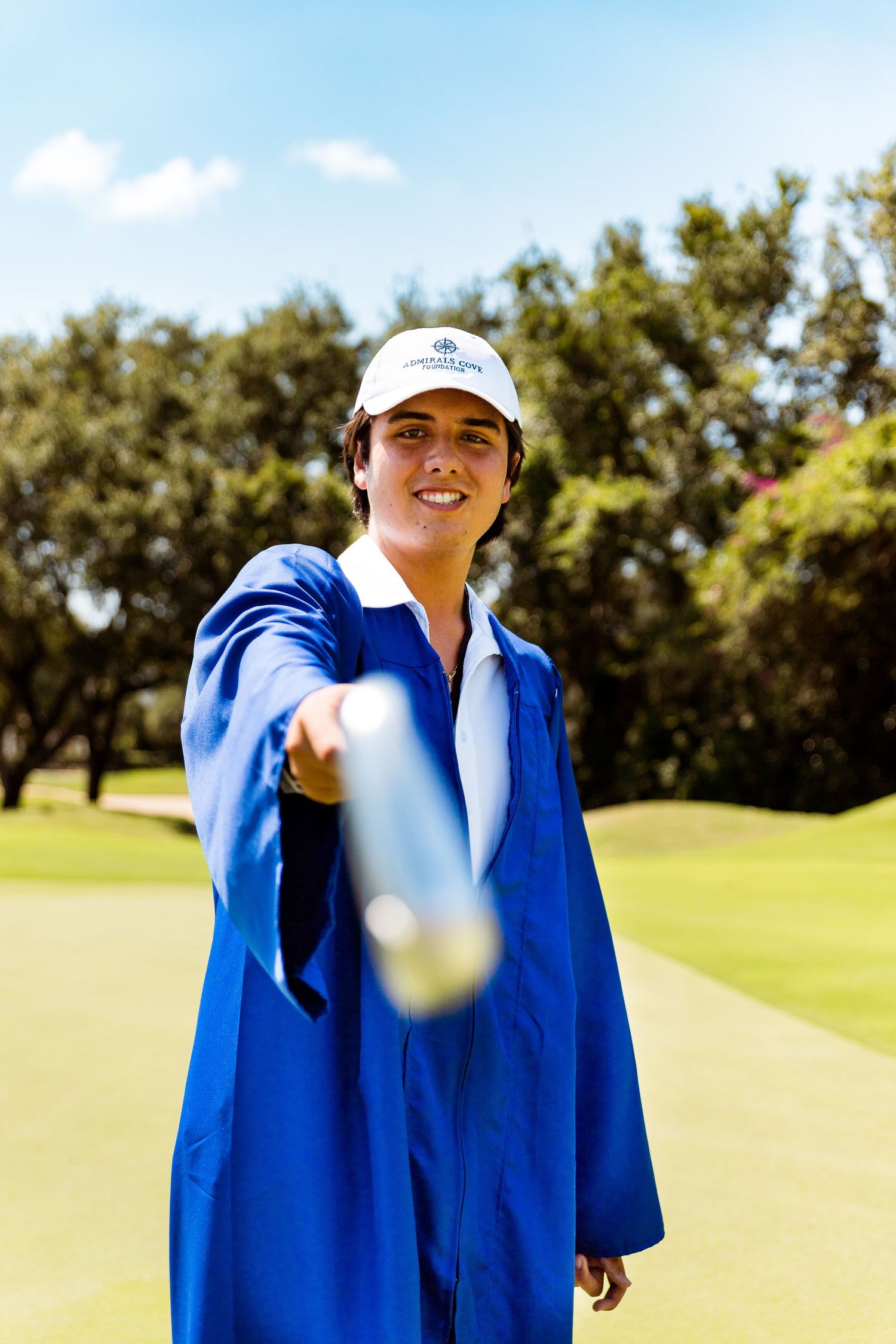 A person in a blue jacket and white cap holds a golf club on a sunny golf course.