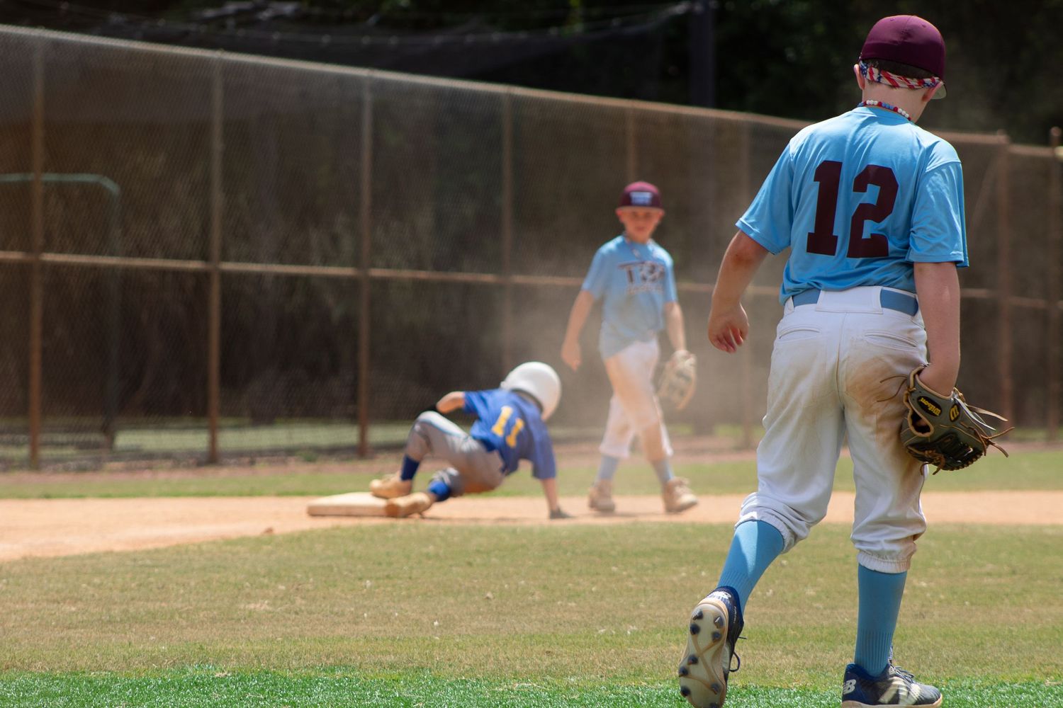 Baseball players in action with sliding play at base during youth game.