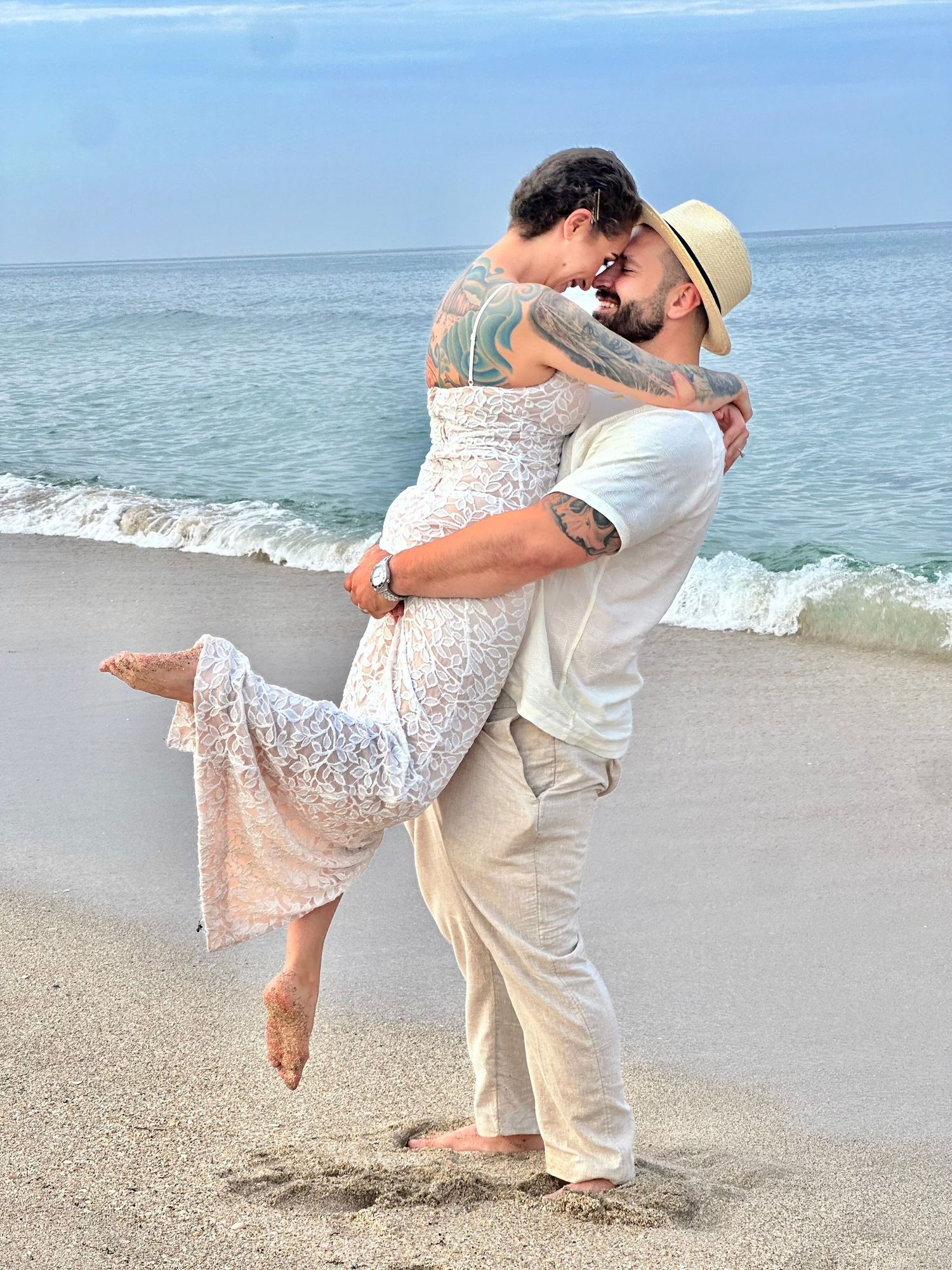 Couple in white embracing romantically on a sandy beach.