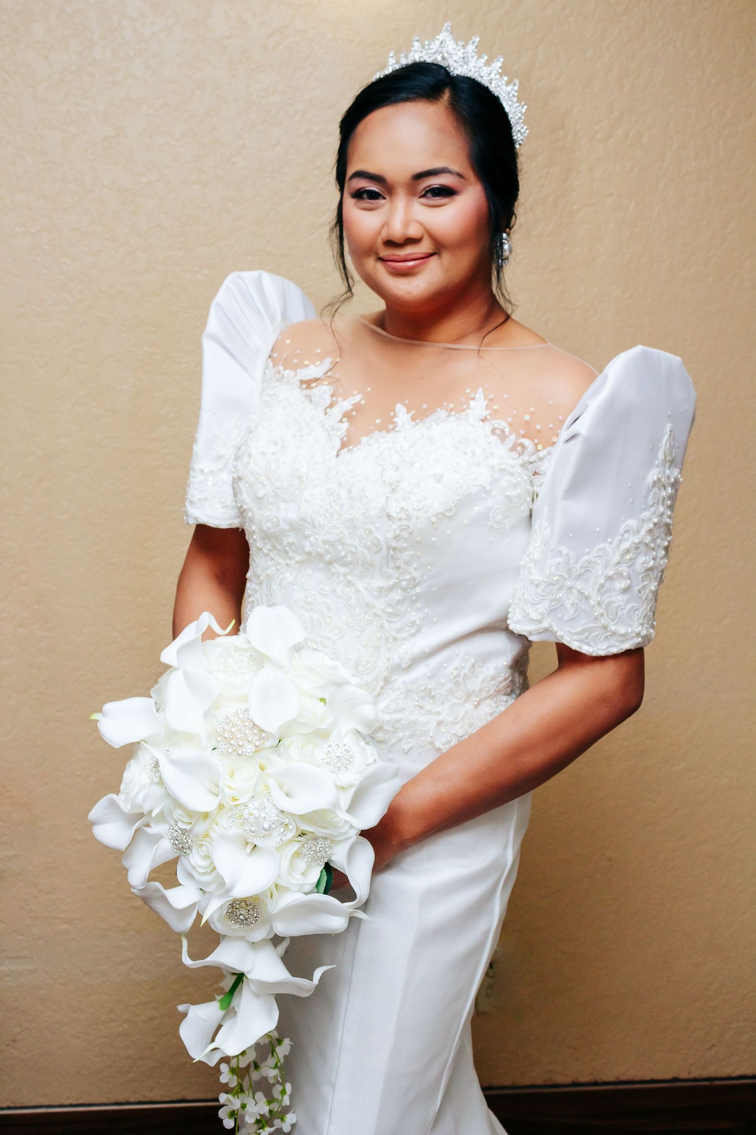 A bride in a white lace wedding dress with puff sleeves holds a cascading bouquet of white orchids.