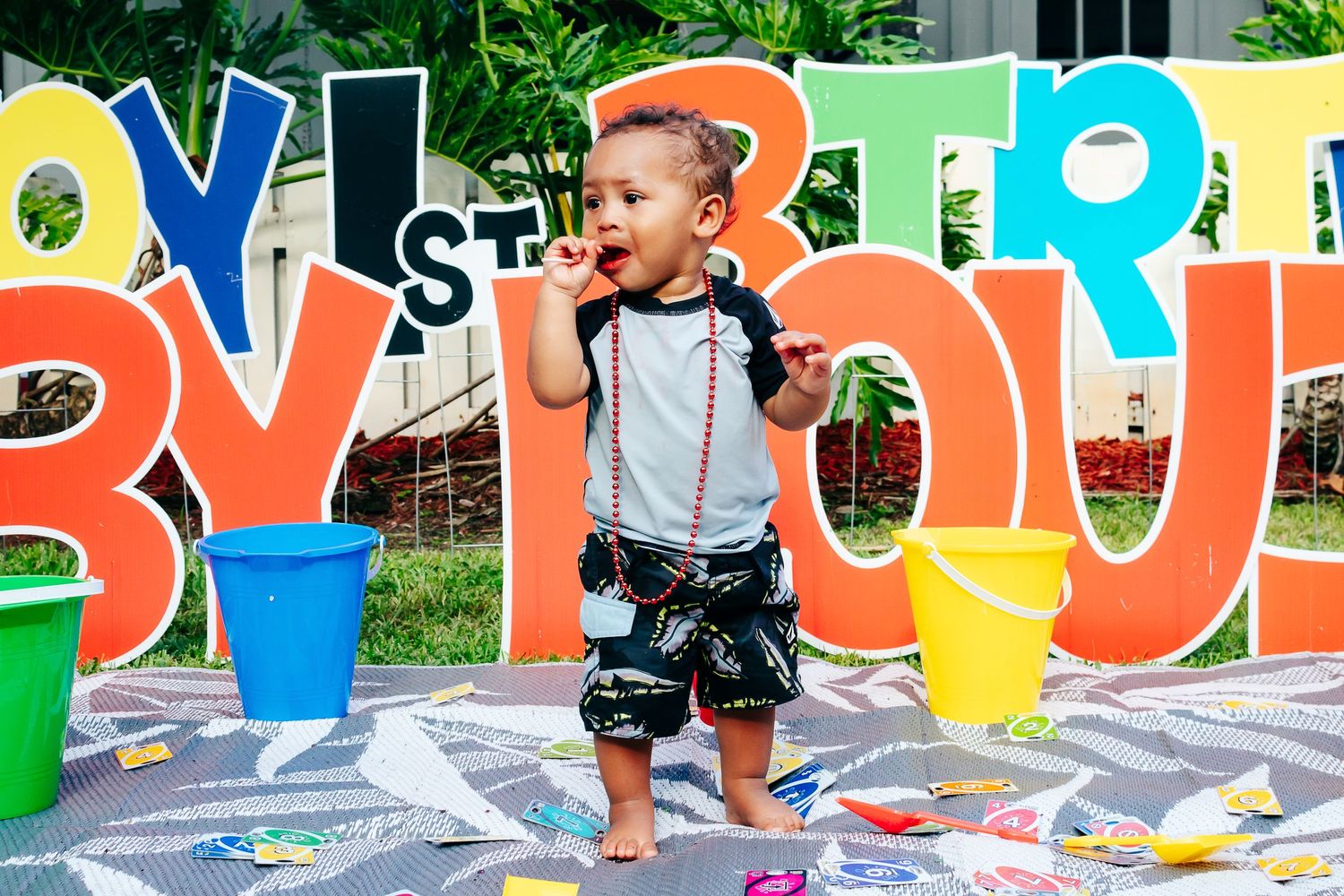 Young child standing in front of colorful letter decorations at an outdoor party.