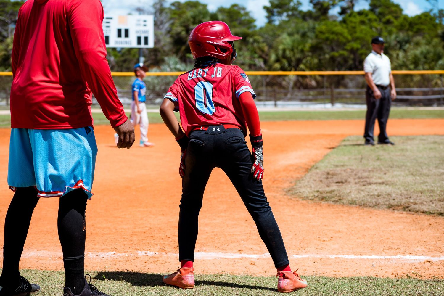 Baseball player in red uniform and helmet takes lead off first base during game.