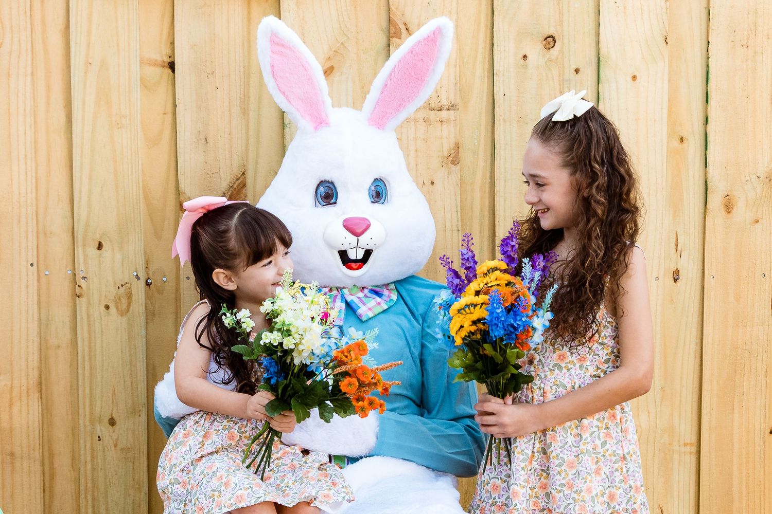 Easter bunny mascot and visitors holding bright spring flower bouquets against wooden backdrop.