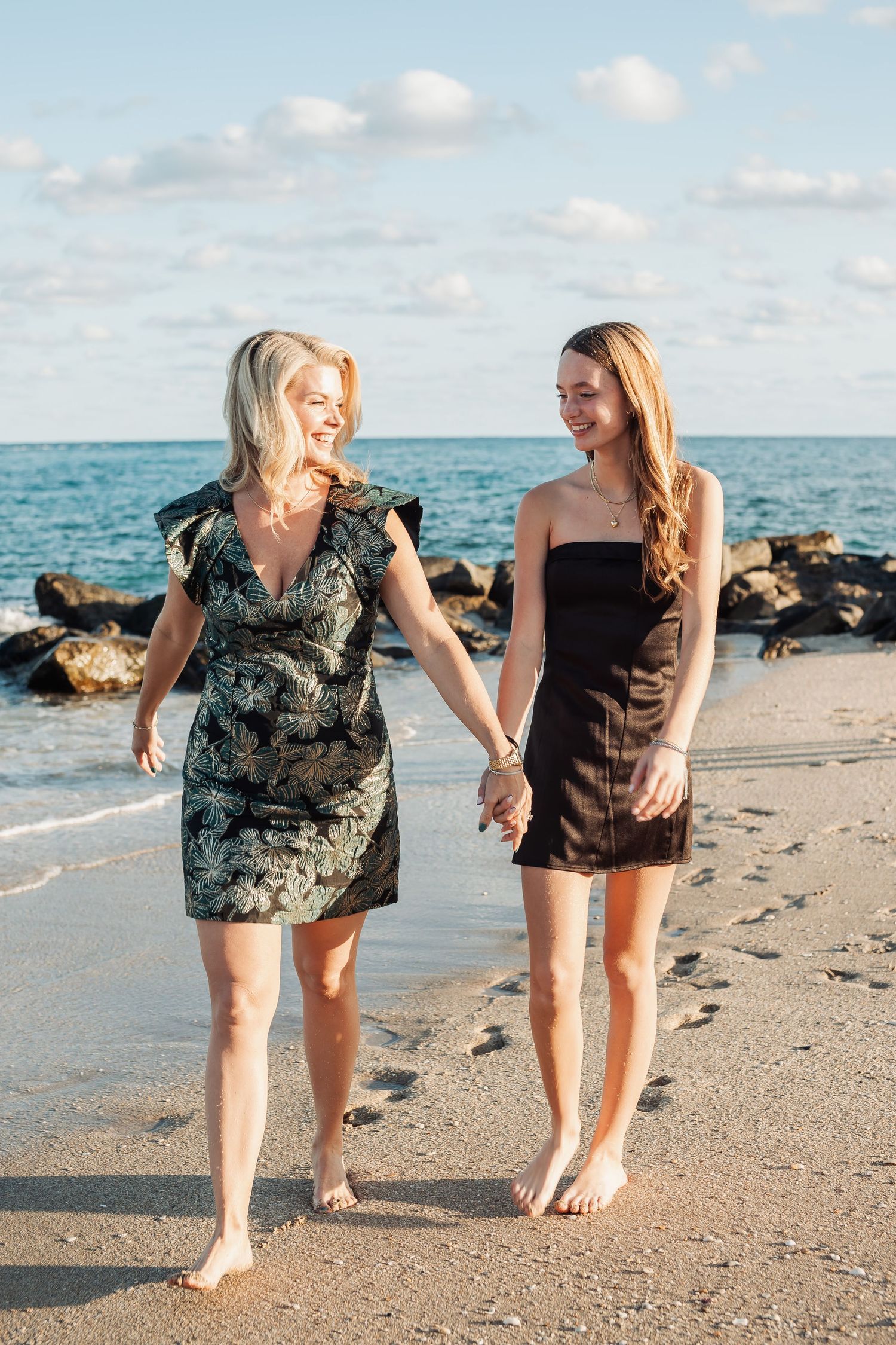 Two people sharing a laugh while walking along a scenic beach with waves crashing on rocks.